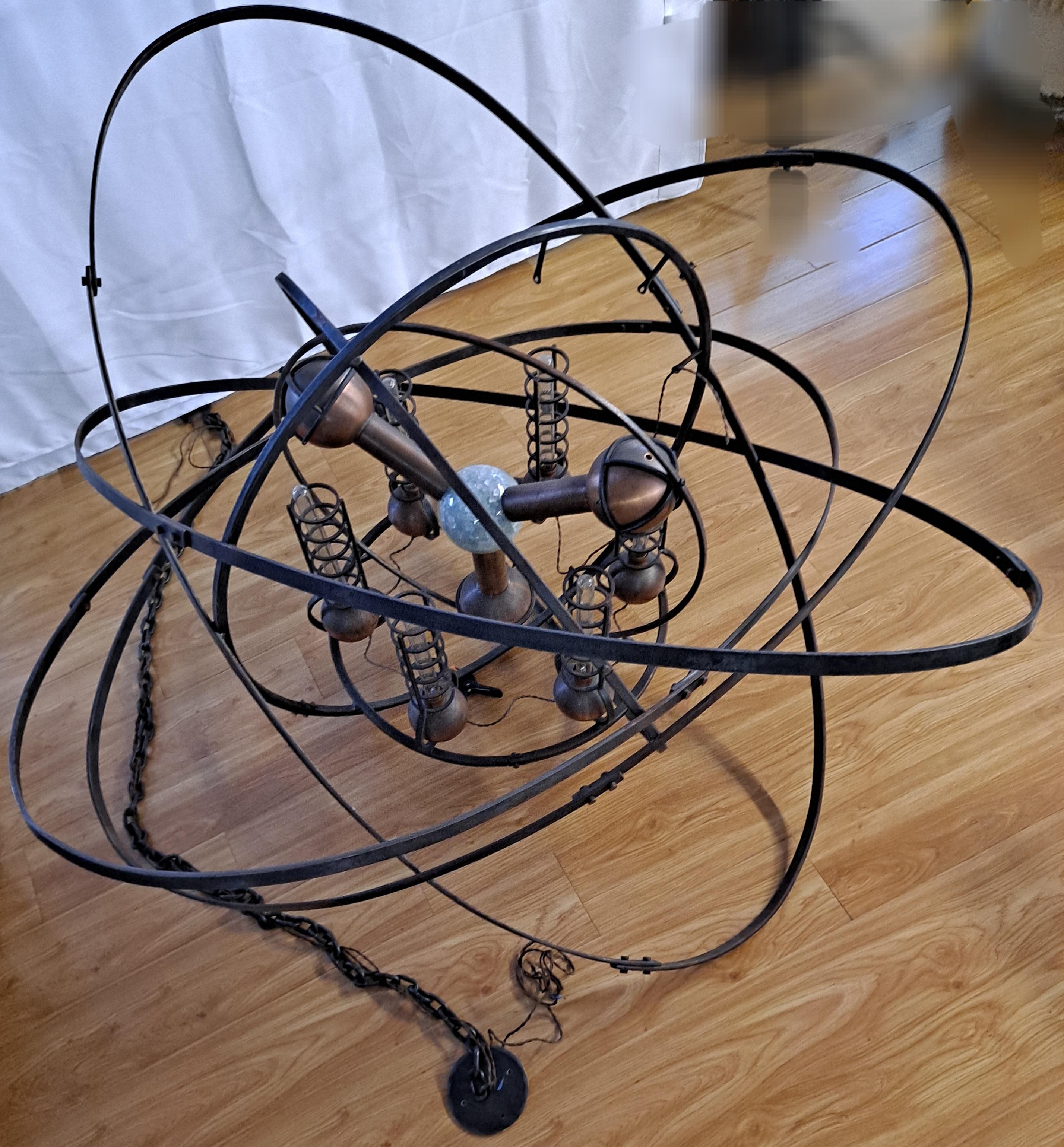 Questo spettacolare lampadario di ispirazione steampunk è stato realizzato a mano dal rinomato fabbro di San Francisco Jefferson Mack.  Una creazione della sua Jules Verne Collection, la cui struttura in ferro ebanizzato ha la forma di un atomo con