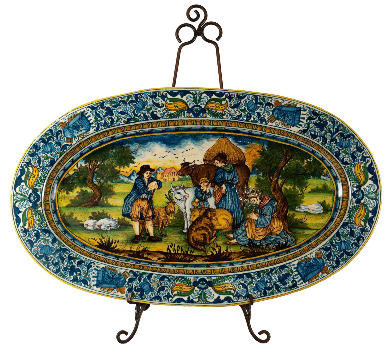 A monumental hand painted Italian Maiolica platter. Border with foliate design surrounding quivers of arrows, center reserve with a figural scene of peasants with their livestock resting under a tree.