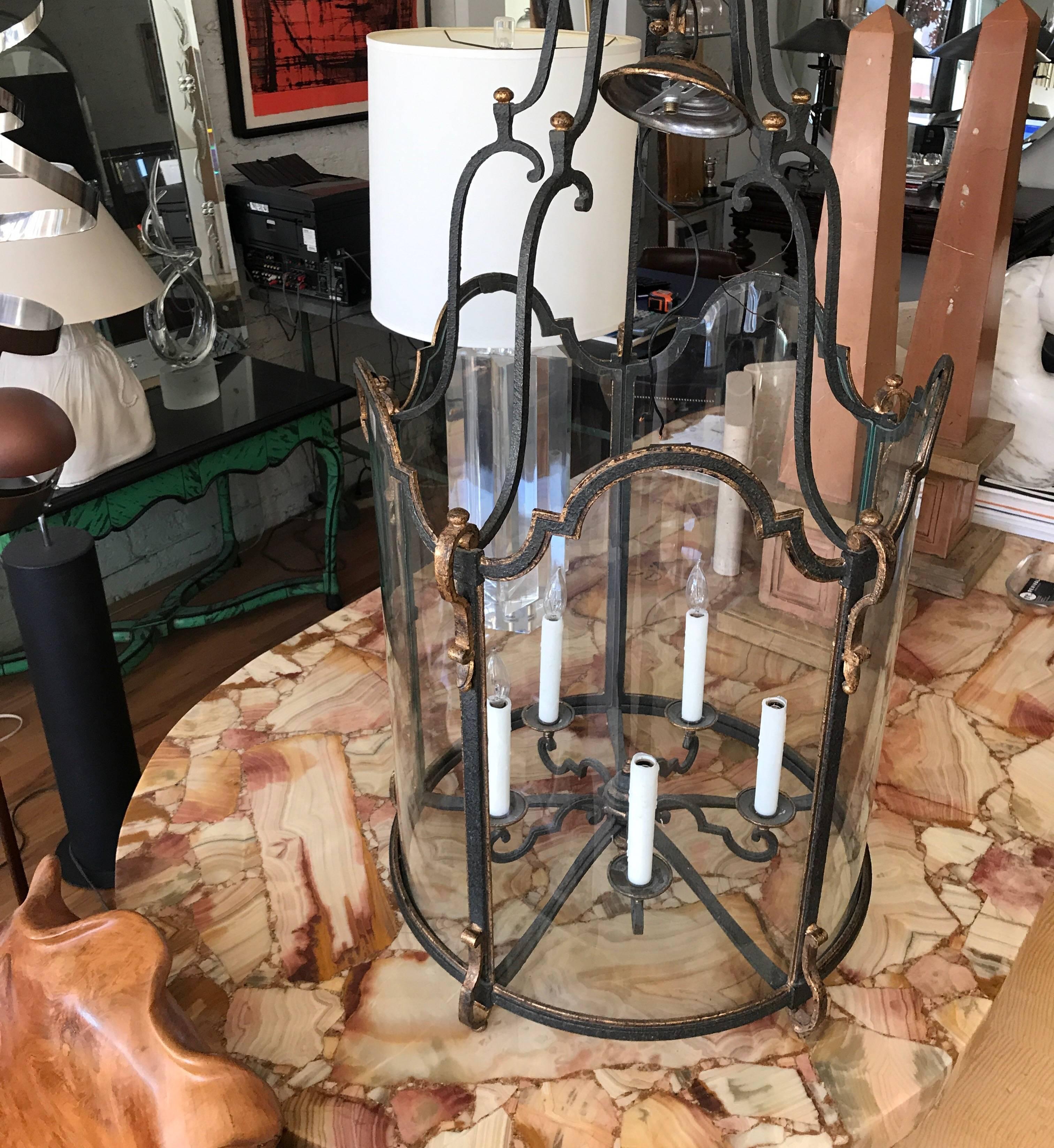 Large scale hand wrought iron and glass hanging center hall lantern. The iron is accented with gilt. 
This Louis XVI style chandelier has imposing proportions. The curved glass is handblown.