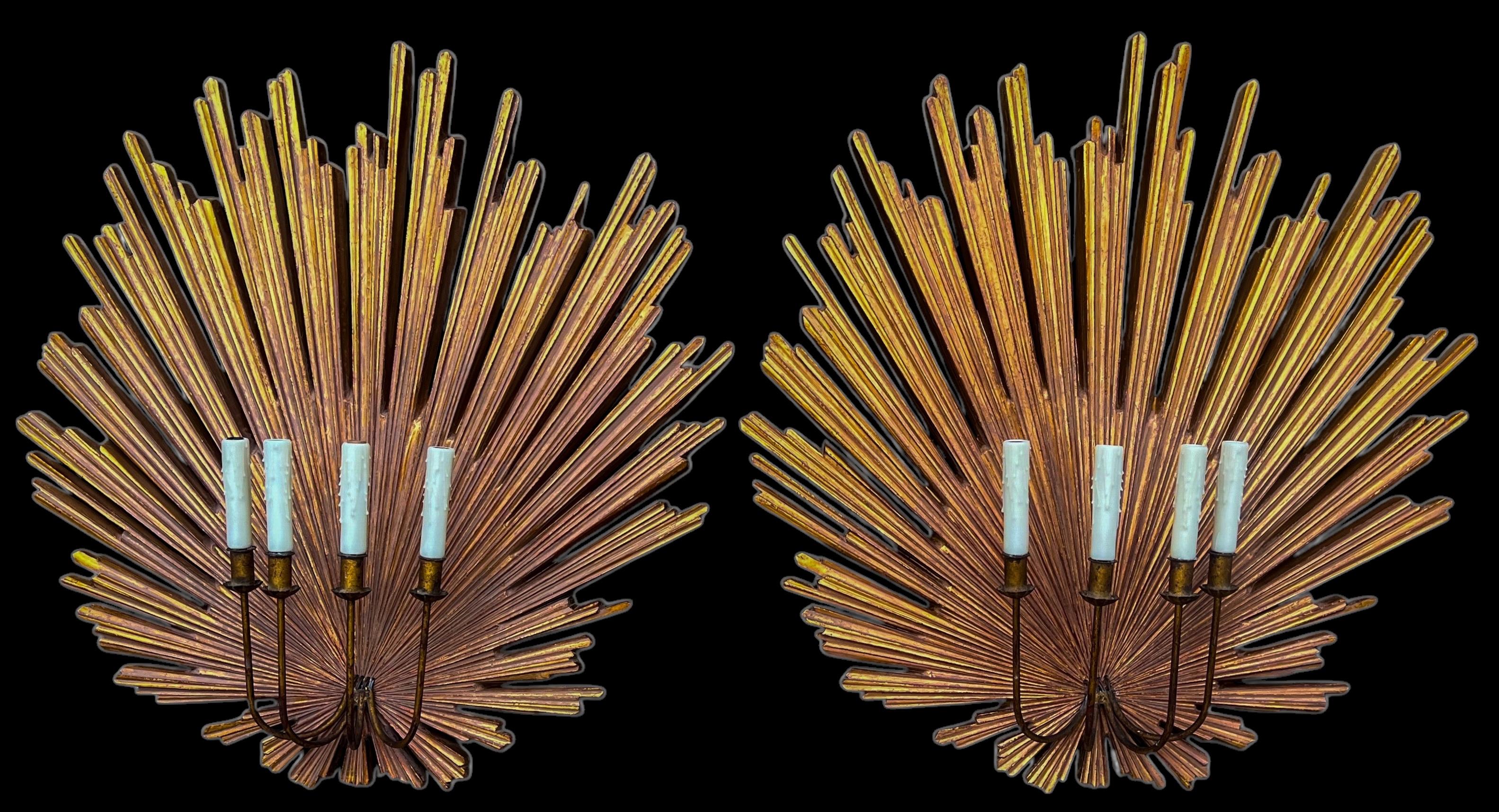 This is a monumental pair of Hollywood Regency style gilded sunburst wall sconces. The wiring is new. Each sconces has four arms and a wax candle cover. The sunburst portion is composition. 