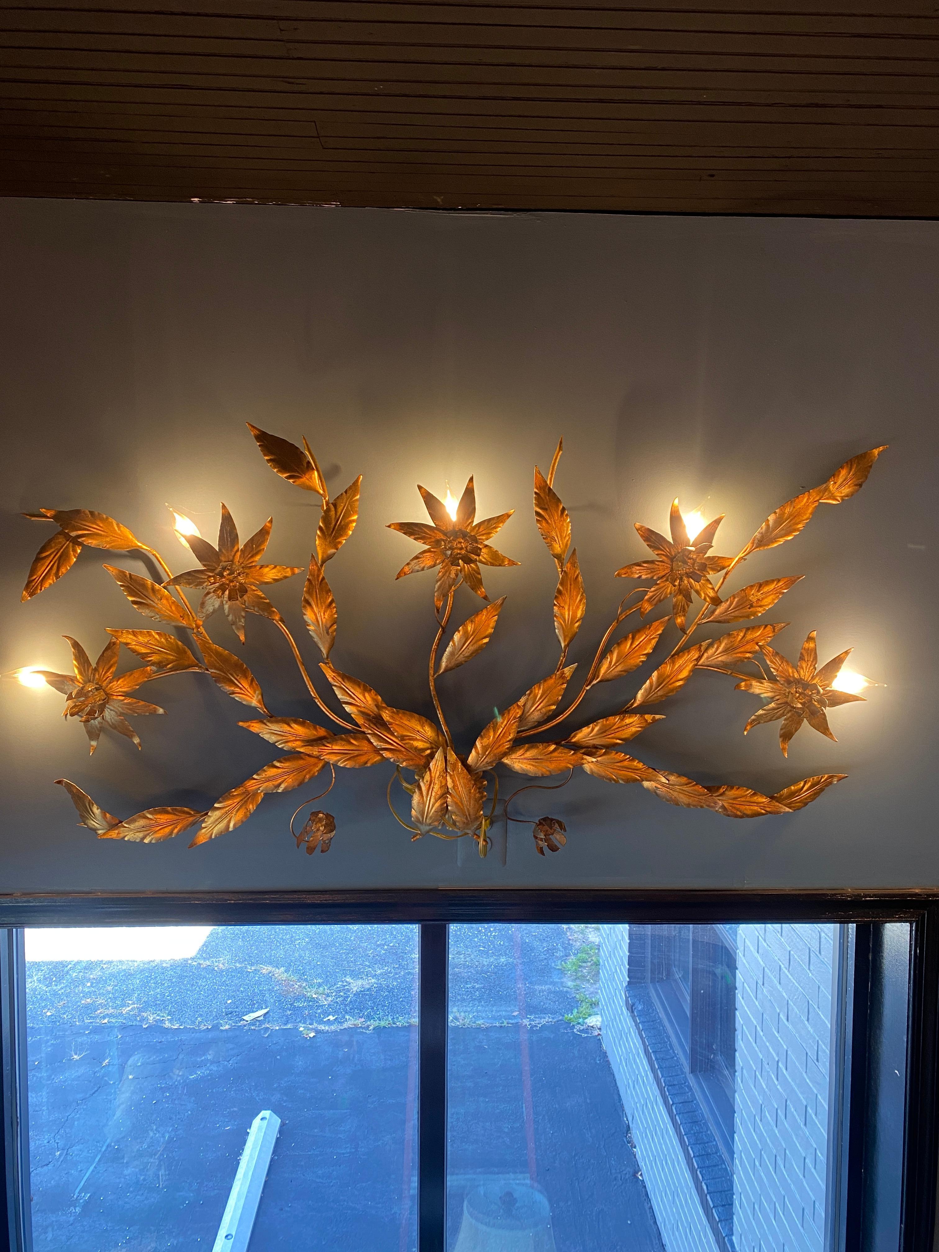 A monumental Hollywood Regency gilt tole wall sconce in floral and leaf form. Three light settings with a total of five lights. Fantastic center wall lighting feature.