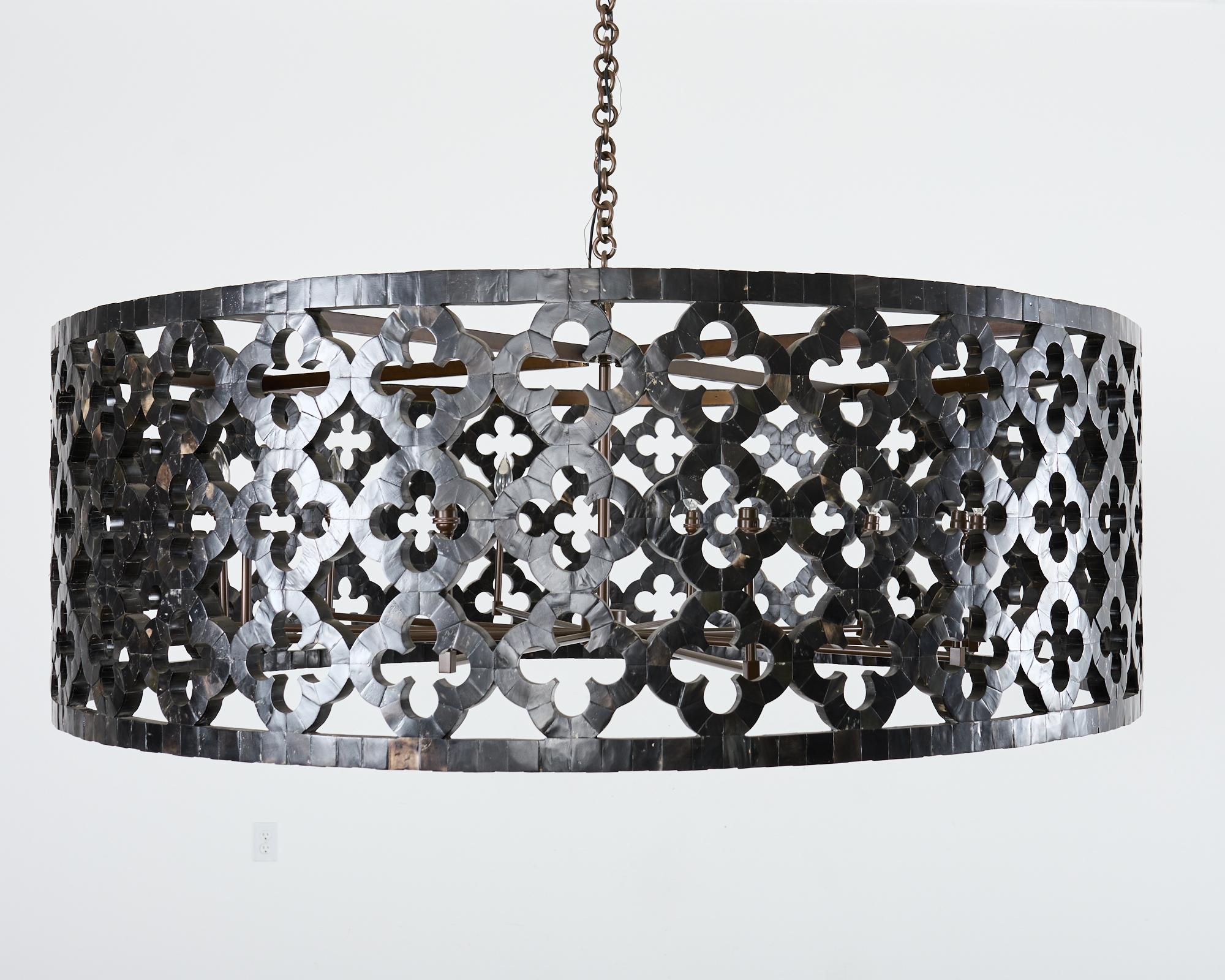 Dramatic monumental sized ten-light drum form chandelier or pendant light featuring an intricate tessalated horn veneered exterior. The chandelier has a round frame decorated with quatrefoil designs and Moorish arabesque shapes. The frame has a dark