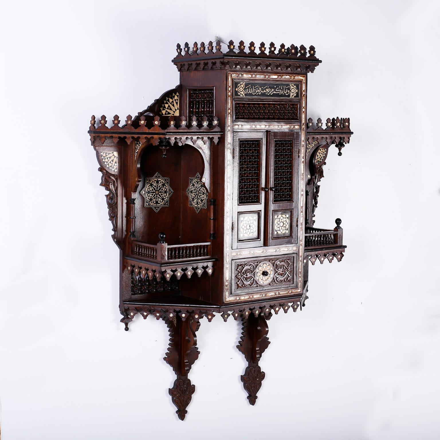Antique Moroccan wall cabinet crafted in mahogany and featuring turrets, Moorish arches, columns, balustrades, inlaid mother of pearl, ebony and bone medallions, floral carvings and an overall generous scale. Best of its kind.