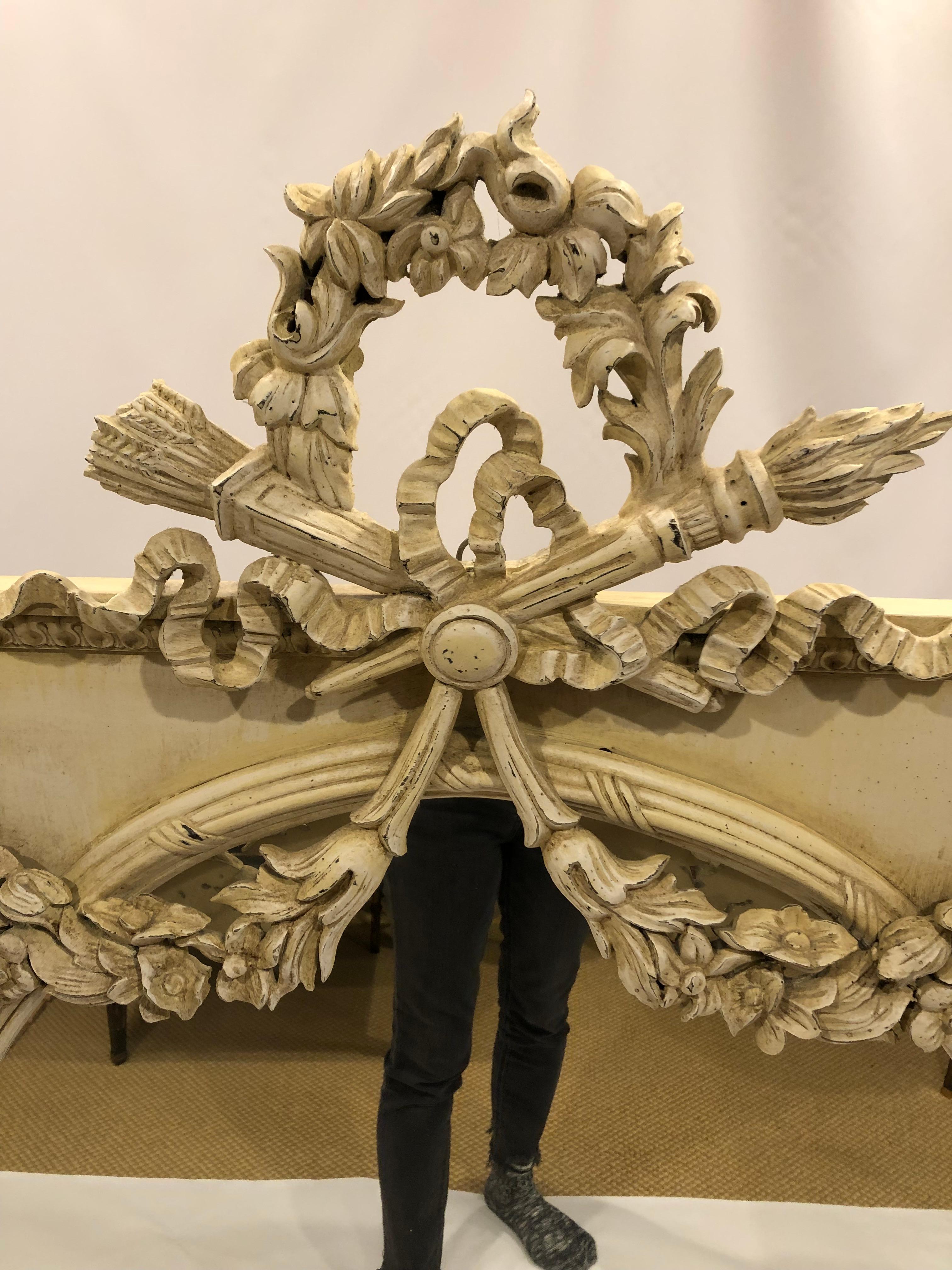 Very large and fancy antique cream painted carved wood mirror in the French style having ornate bows and garlands on the frame and oval mirror. Mirror itself is 28 W x 38 H.