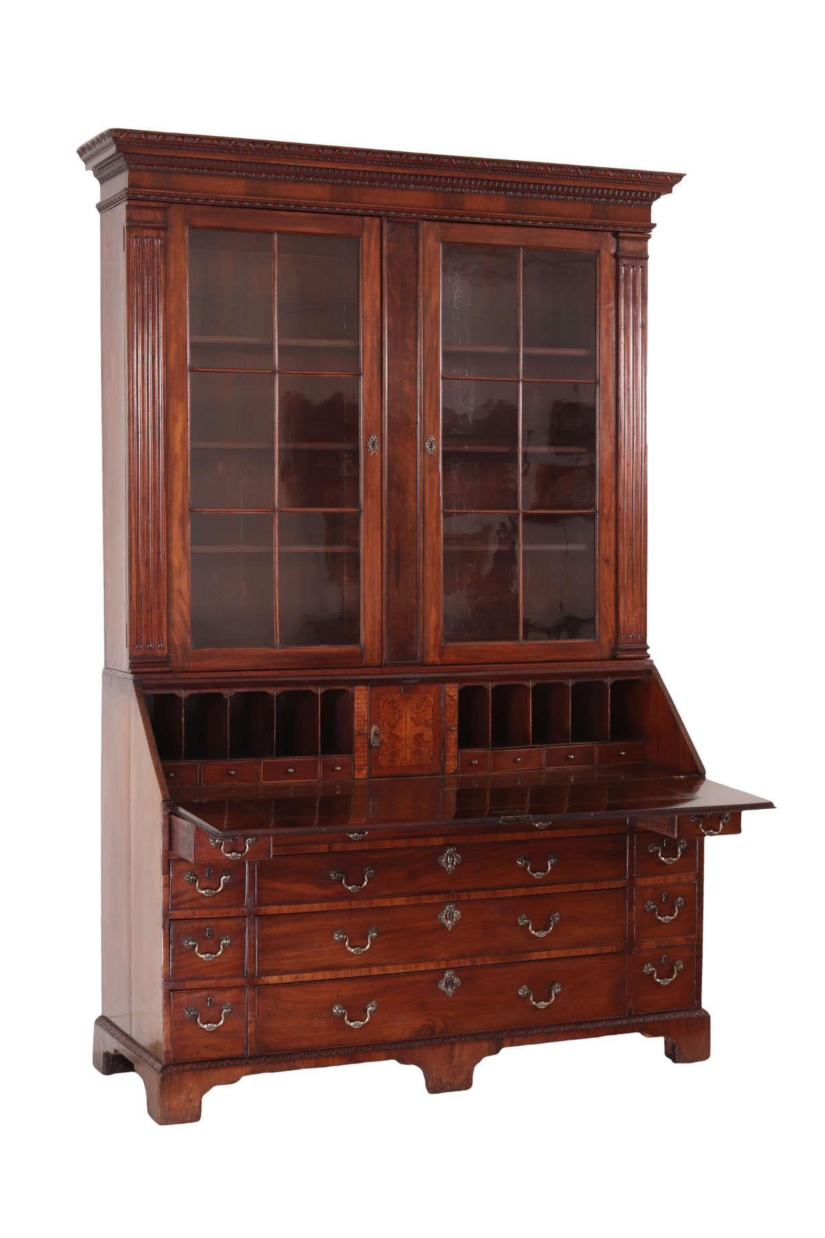 Large Irish George III mahogany secretary bookcase, the upper portion with an elaborate cornice carved with trailing shells, dentils and foliate moldings. The glazed doors with engaged fluted pilasters open to three fixed shelves. The desk portion