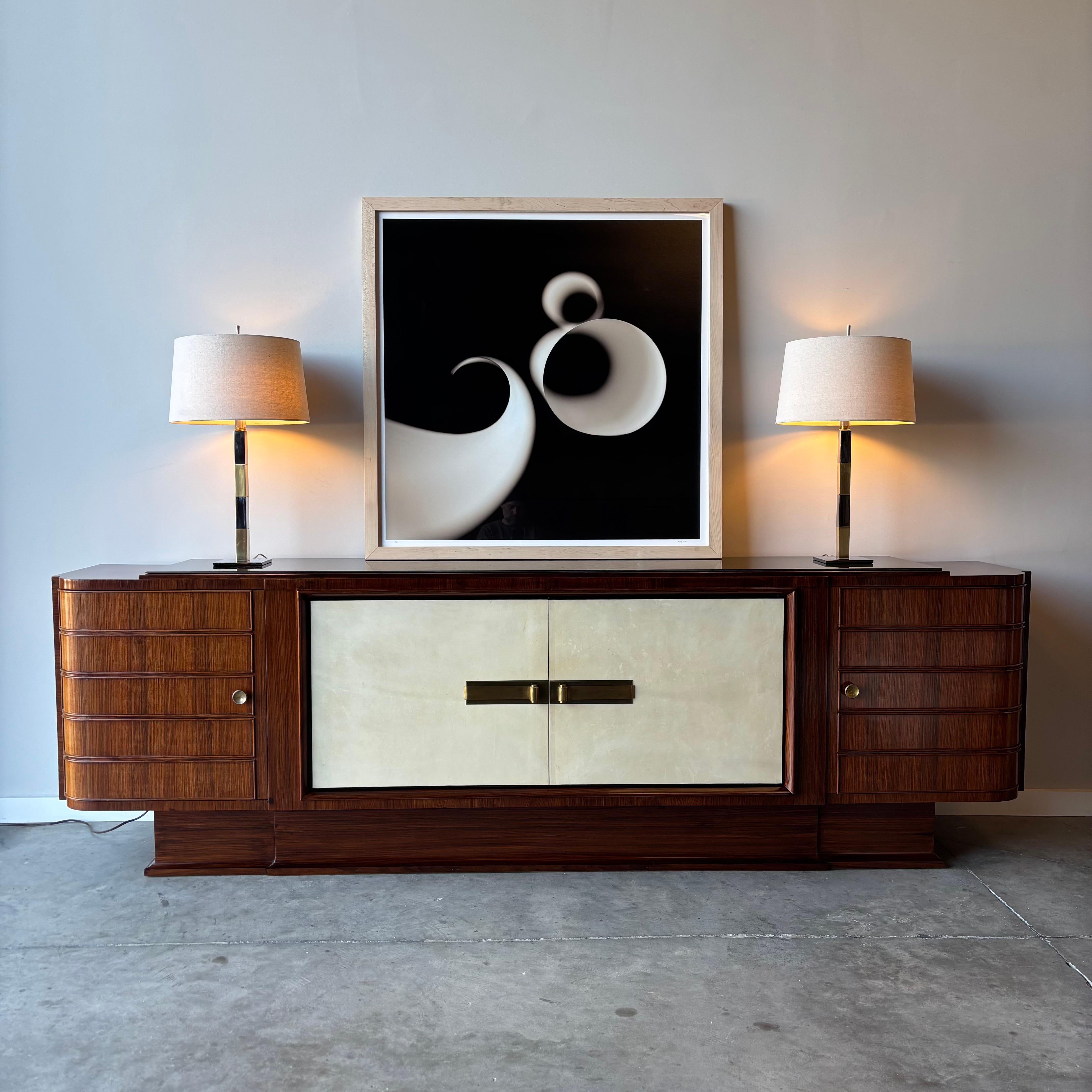A stunning rosewood credenza dating to the 1930s, Italy.  With obvious cues from Jules Leleu this incredible cabinet features a mahogany case with rosewood veneer and goatskin parchment clad doors.  Magnificent scrolling brass handles and plenty of