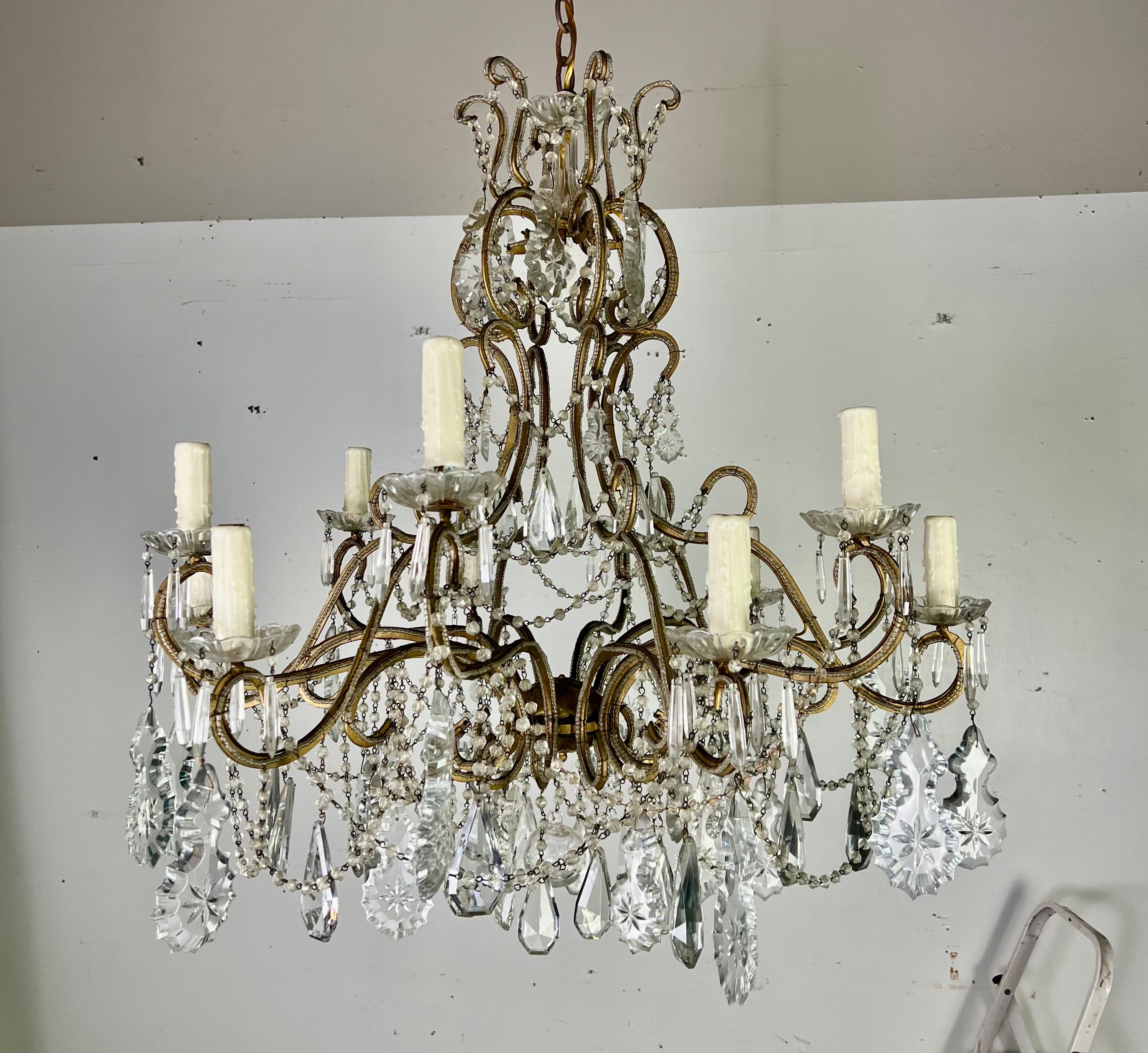 Lampadario a 12 luci con perline in cristallo italiano di dimensioni monumentali.  Questo lampadario è un apparecchio vintage decorato con una struttura in metallo dorato con intricate volute.  Ha 12 braccia, ognuna delle quali regge una candela di