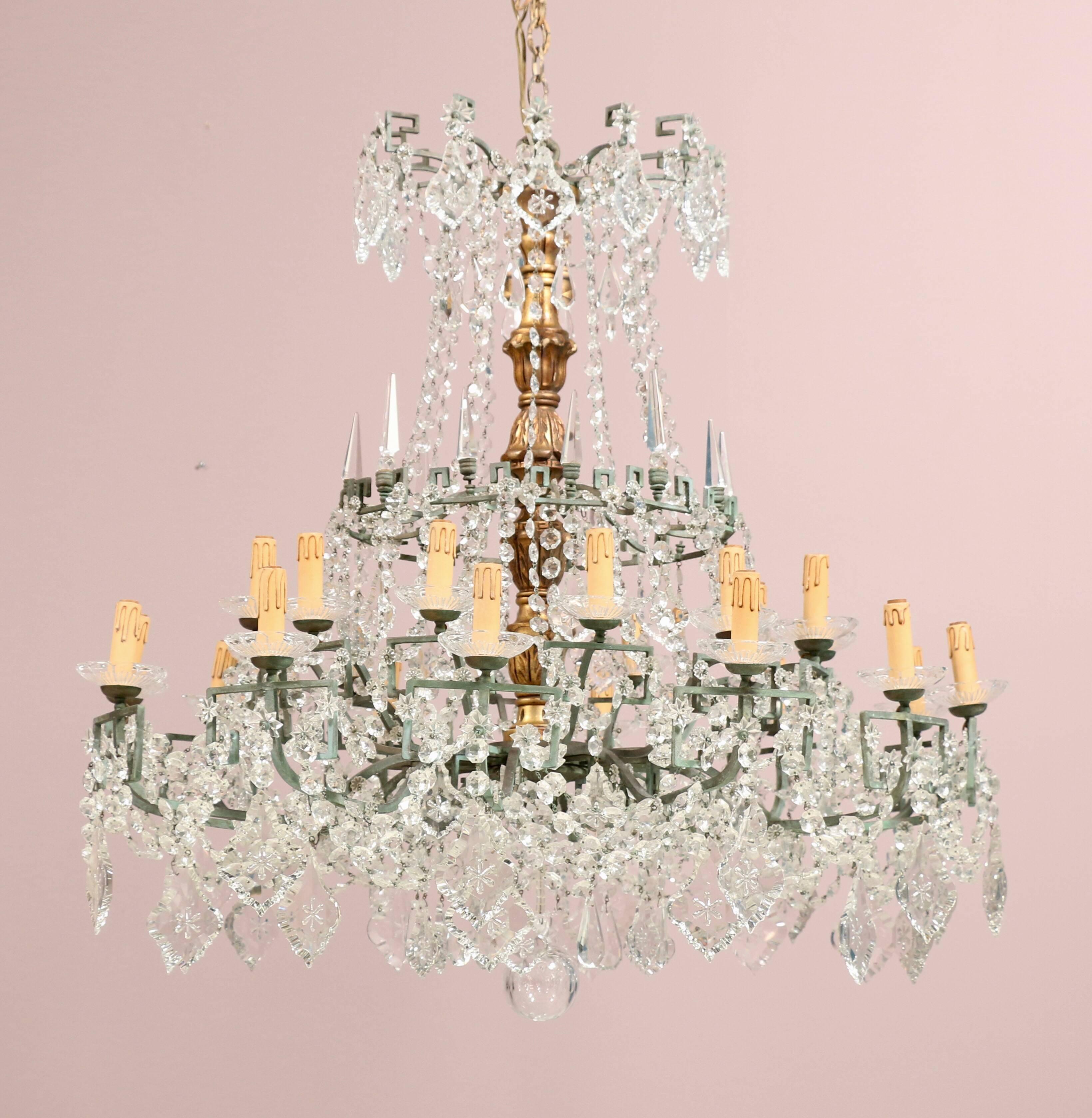 Majestic 1940s, Italian crystal, gilt-wood and bronze two-tier chandelier in the Neoclassical style. The chandelier is composed of a gilt-wood center column, a bronze frame with a Greek key motif and and an abundance of crystal beads and prisms (in