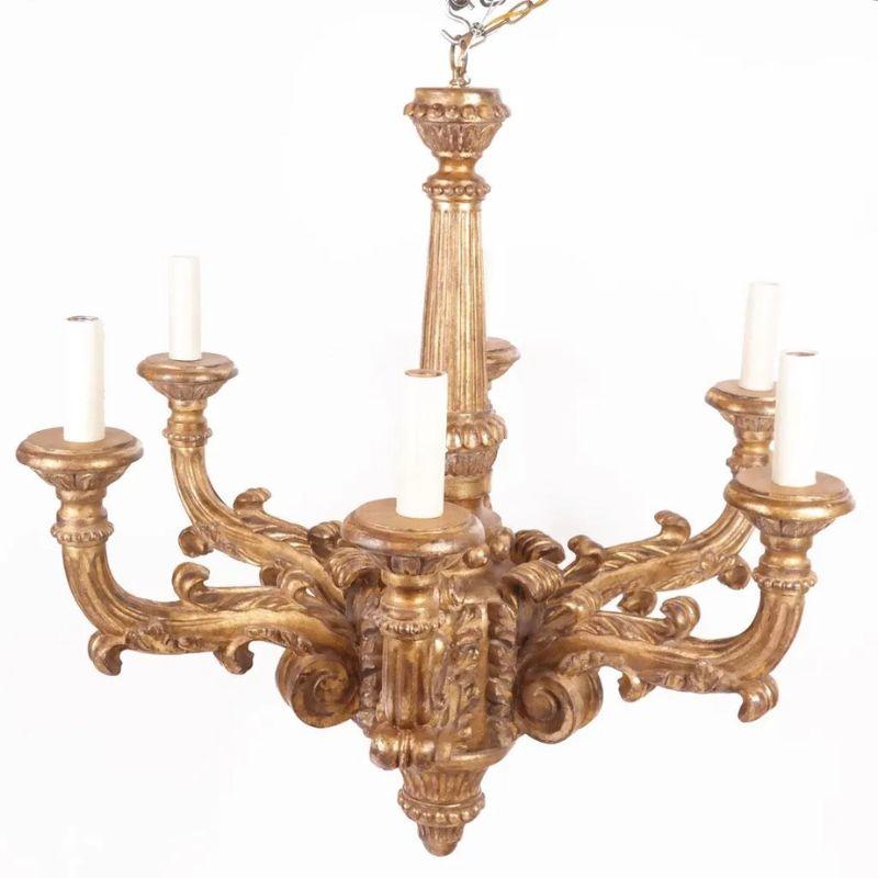 A monumental Italian giltwood six arm chandelier, circa 1940.  The chandelier is carved with intricate details that include scroll arms, curved leaves, bead detail and fluted carving. The grand gold chandelier will make an important statement and