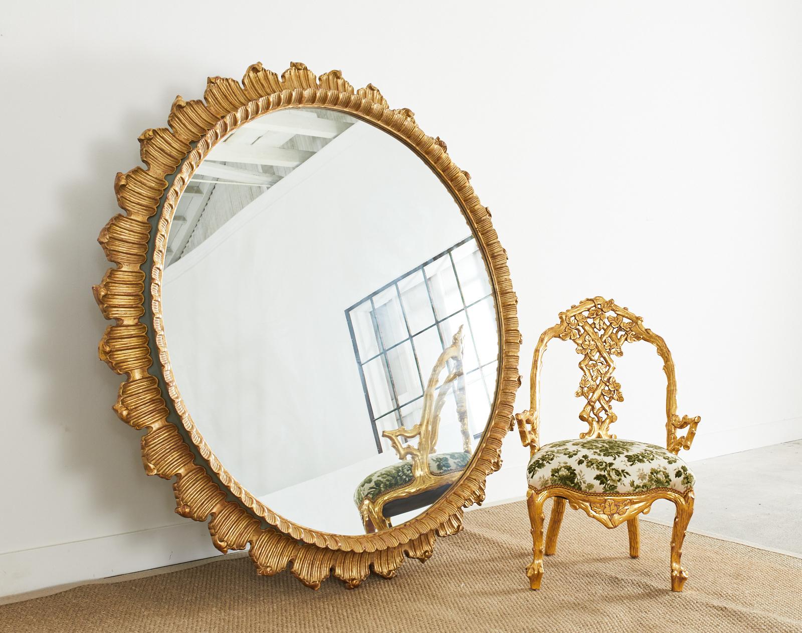 Fantastic Italian giltwood sunburst wall mirror made with monumental porportions and scale. Measuring nearly 68 inches wide with a carved frame having a neoclassical style rocaille shell motif outer border and a raised thinner gilt inner border. The
