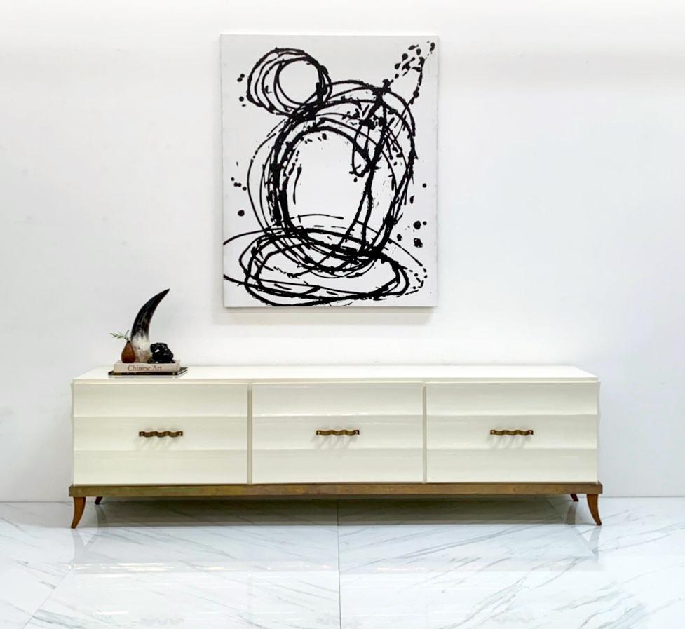 This piece is absolutely stunning. A monumentally large credenza in the style of Tommi Parzinger, this credenza features a scalloped ivory lacquered body with solid brass Italian modern style squiggly brass door pulls, aged brass bottom framing, and