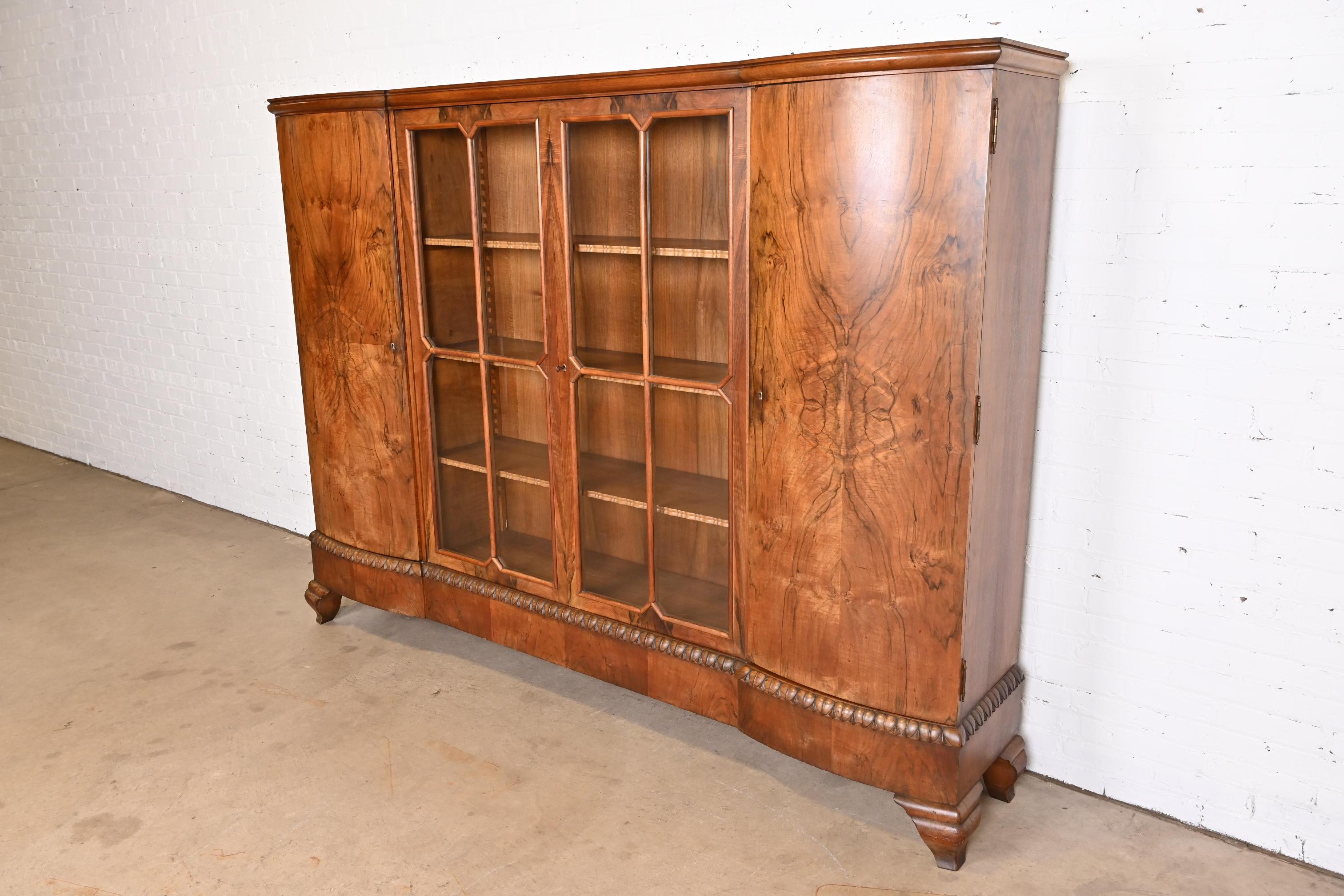 A stunning monumental French Art Deco knockdown bookcase or bar cabinet

In the manner of Jules Leleu

France, Early 20th century

Gorgeous book-matched burled walnut, with carved trim and mullioned glass front doors. Interior shelving is