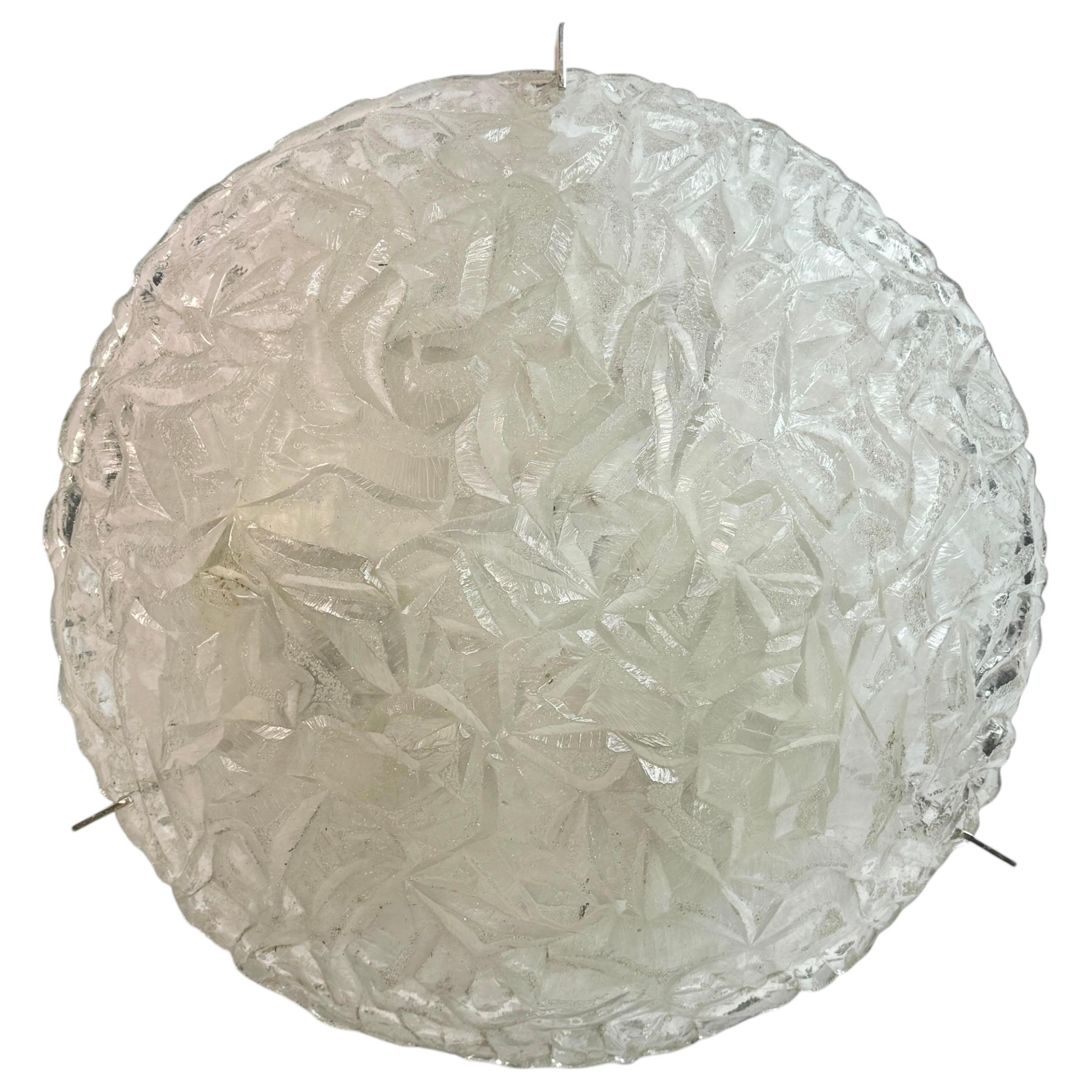 Runde Deckenleuchte aus Glas mit Eisblockmuster von Kaiser Leuchten, Deutschland, 1970er Jahre.
Der schwere Schirm besteht aus einem einzigen Stück dickem Klarglas, das um einen weißen Metallrahmen gefaltet und mit drei Stahlschrauben befestigt ist.