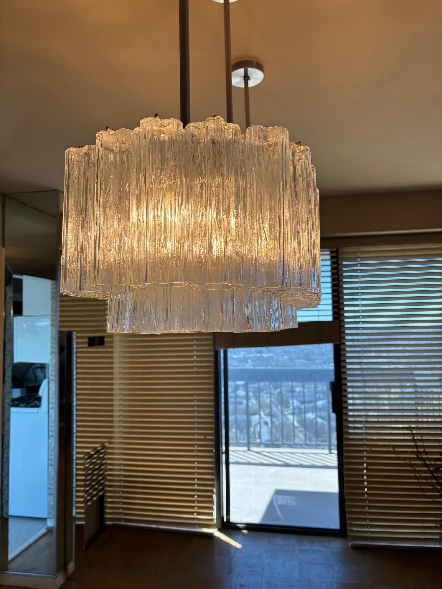 Suggestivo e sofisticato, questo lampadario a tubo Kalmar Tronchi vintage di grandi dimensioni attira l'attenzione con la sua presenza scultorea e la sua squisita fattura. L'apparecchio è caratterizzato dall'alternanza di tubi Tronchi in vetro