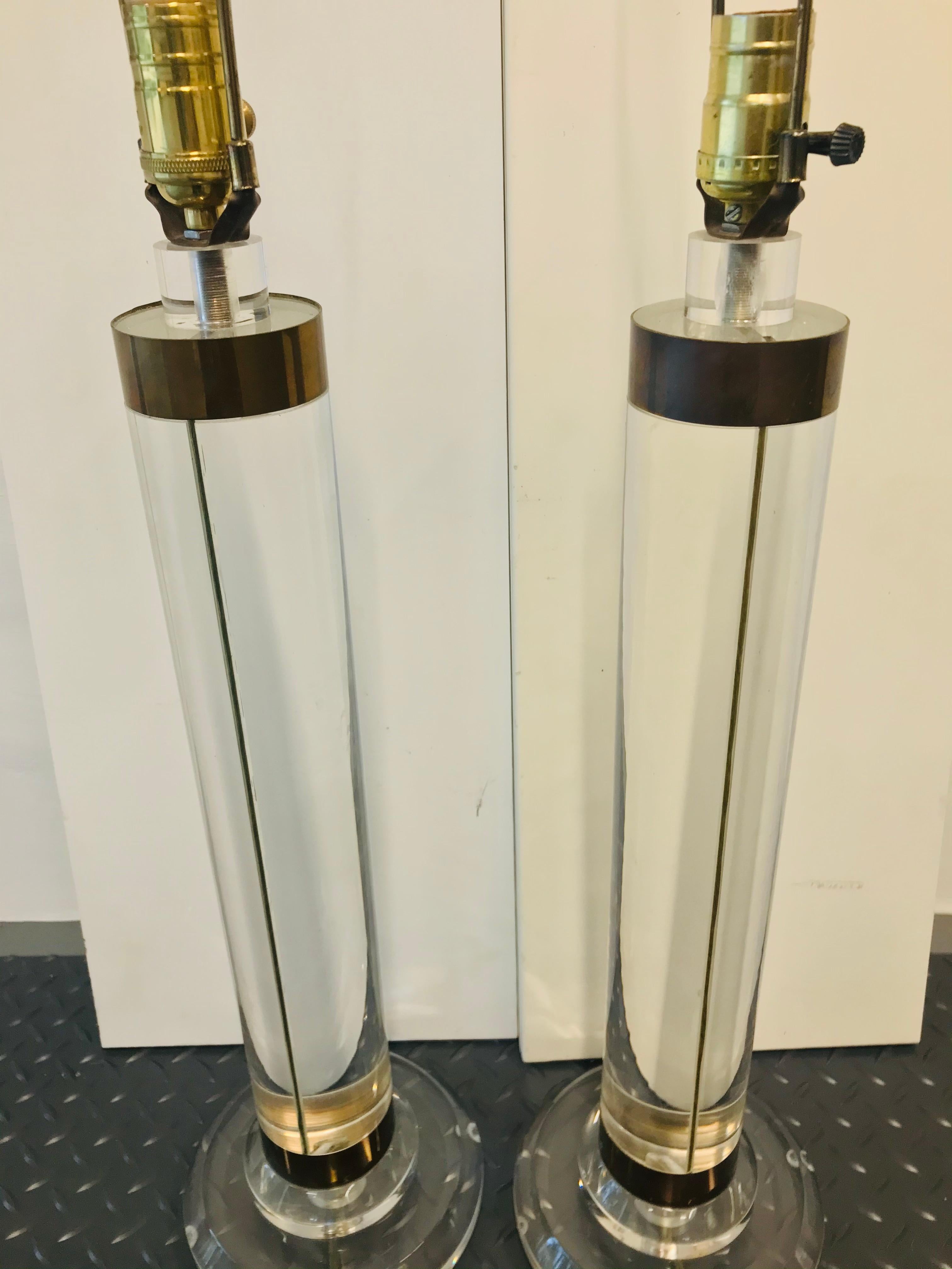 Gorgeous pair of clear Lucite cylinder table lamps with polished brass banding. Designed by Karl Springer in the 1980s. 
These lamps stand 33