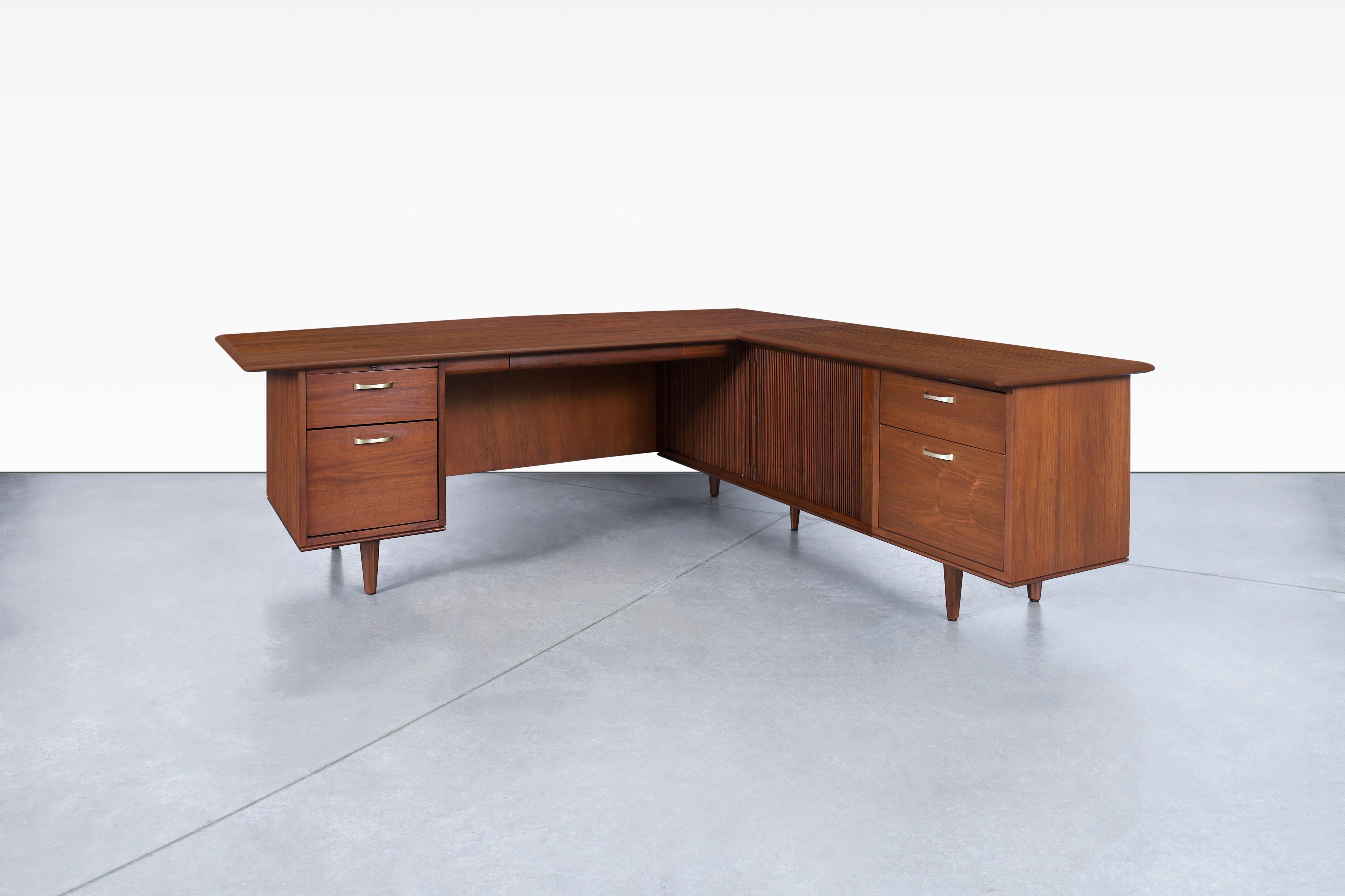 Mid-century L-shaped walnut desk manufactured by Monteverdi Young in the United States, circa 1960s. The boomerang shape adds a unique touch, seamlessly blending style and functionality. The front design is marvelous, featuring two sliding tambour