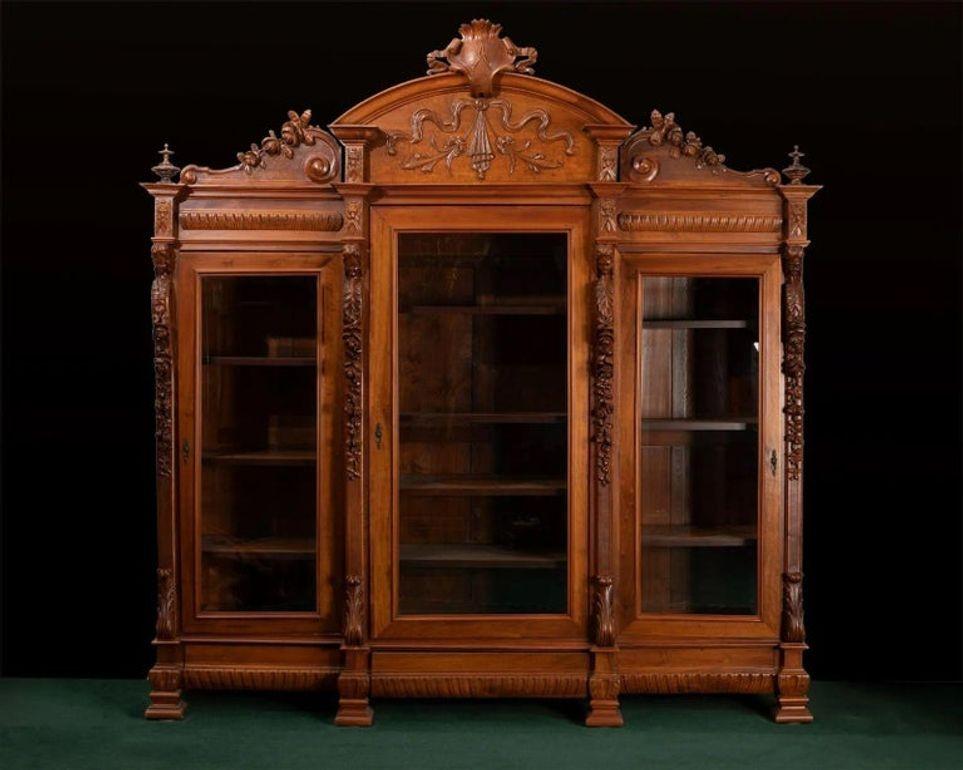 Grande bibliothèque italienne en noyer de la fin du XIXe siècle, délicieusement travaillée avec des sculptures complexes et des proportions élégantes. Cette monumentale bibliothèque à trois portes est dotée de portes en verre biseauté, permettant