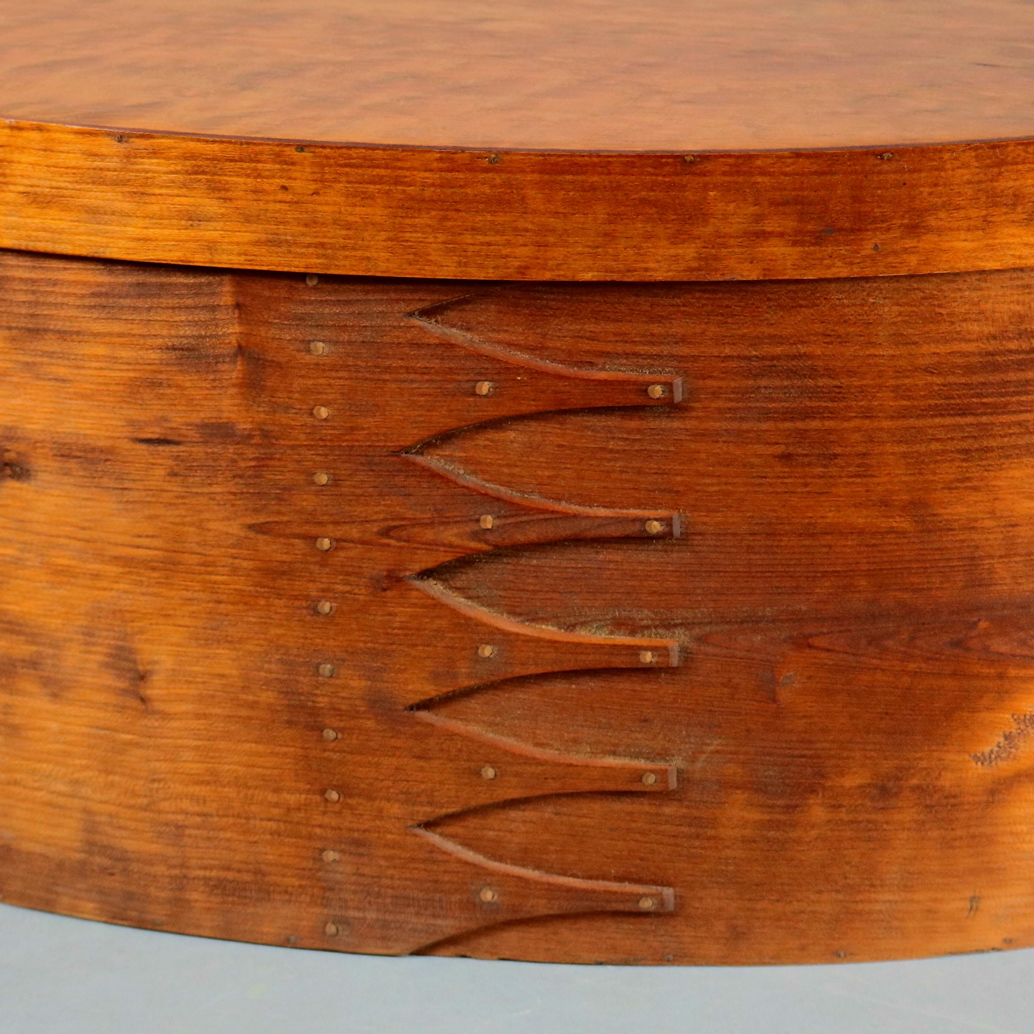 A Lesher School shaker box offers bentwood bird's-eye maple pegged construction in oval form with six Gothic-shaped finger joints (swallowtails) finished in copper tacks, 20th century.

Measures: 11.25