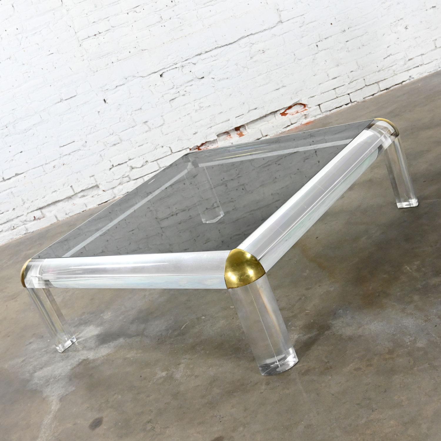 Gorgeous Modern or Hollywood Regency Monumental Lucite bulky square coffee table with smoke glass inset top and brass corner accents attributed to Karl Springer. Beautiful condition, keeping in mind that this is vintage and not new so will have