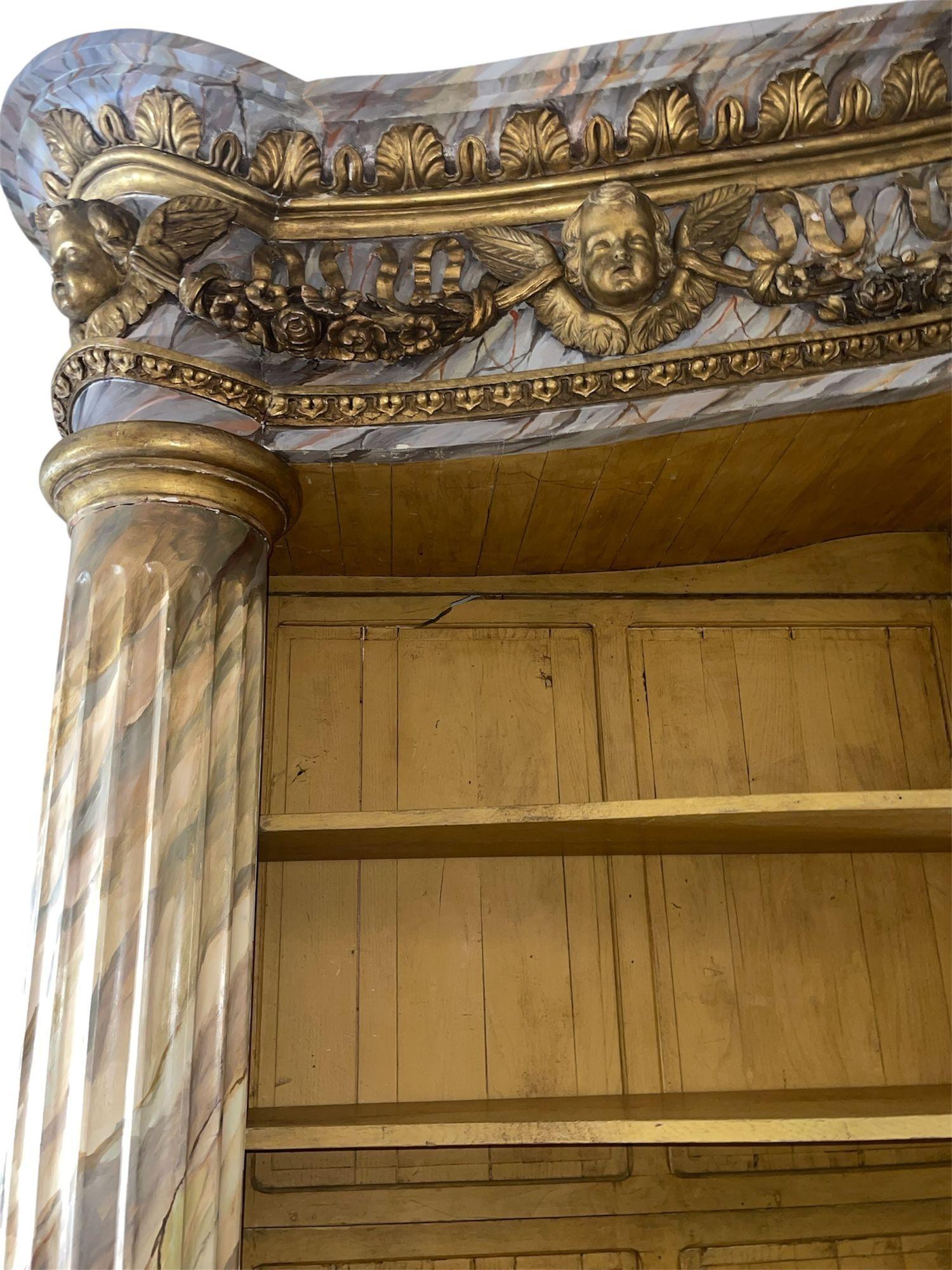 Une impressionnante et monumentale bibliothèque française du milieu du 19e siècle, délicieusement travaillée en bois sculpté avec une peinture en faux marbre et des ornements dorés. La forme architecturale présente trois colonnes cannelées divisant