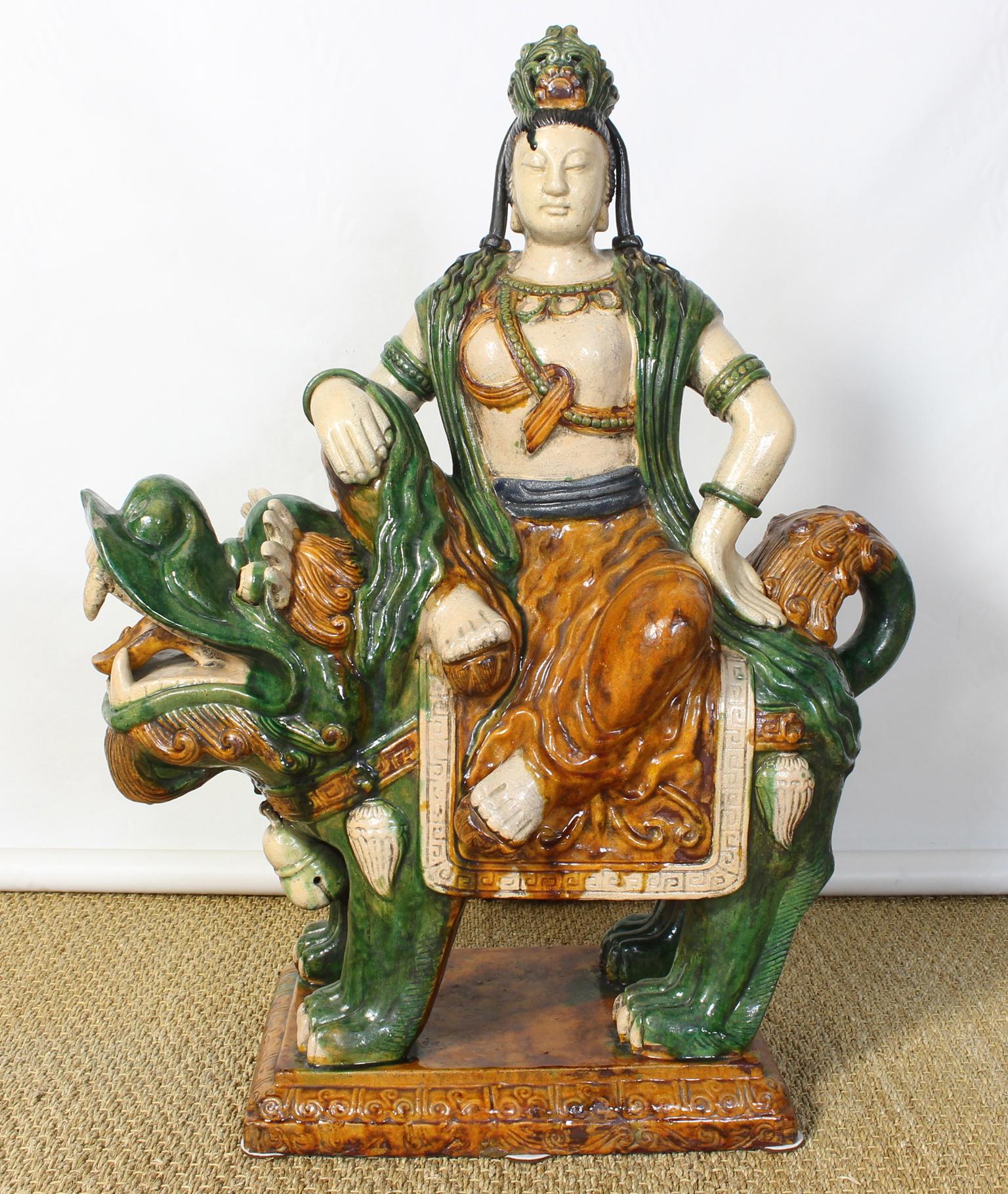 A large and impressive mid-20th century Chinese glazed ceramic polychrome decorated statue of Quan Yin perched upon a foo dog.