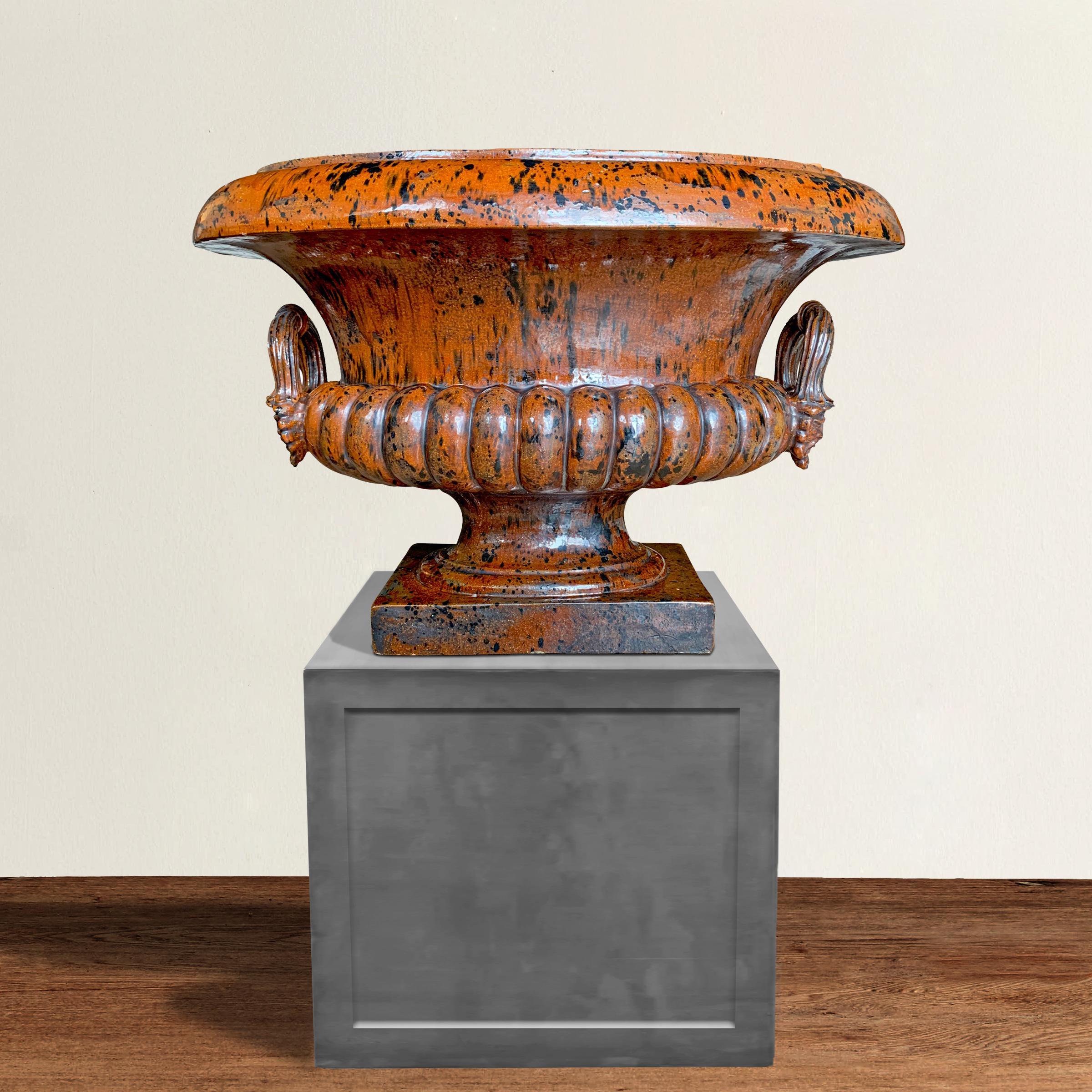 A fantastic monumental Italian mid-20th century tortoise shell glazed ceramic urn of classical form with a thick lip, fluted body, narrow foot, and two applied handles each with two bearded faces. Perfect on its own, or planted with ferns or orchids