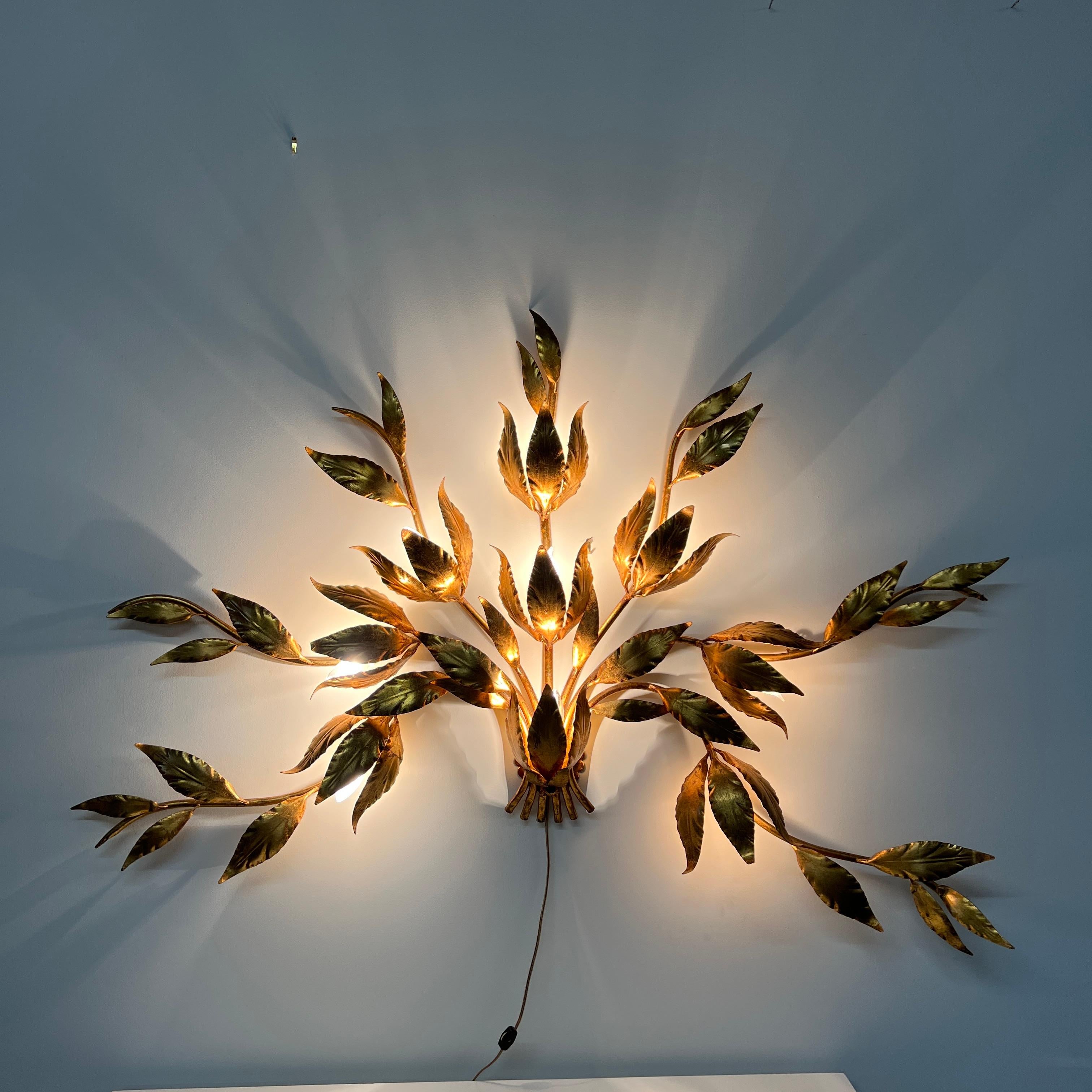 Stunning large gilded wall sconce by Hans Kogl. It has seven arms that have gilded leaves on branches.  Lights are hidden behind certain leaves (there are 9 bulbs).  The gilding is in excellent condition.  On the back of the piece there are a few