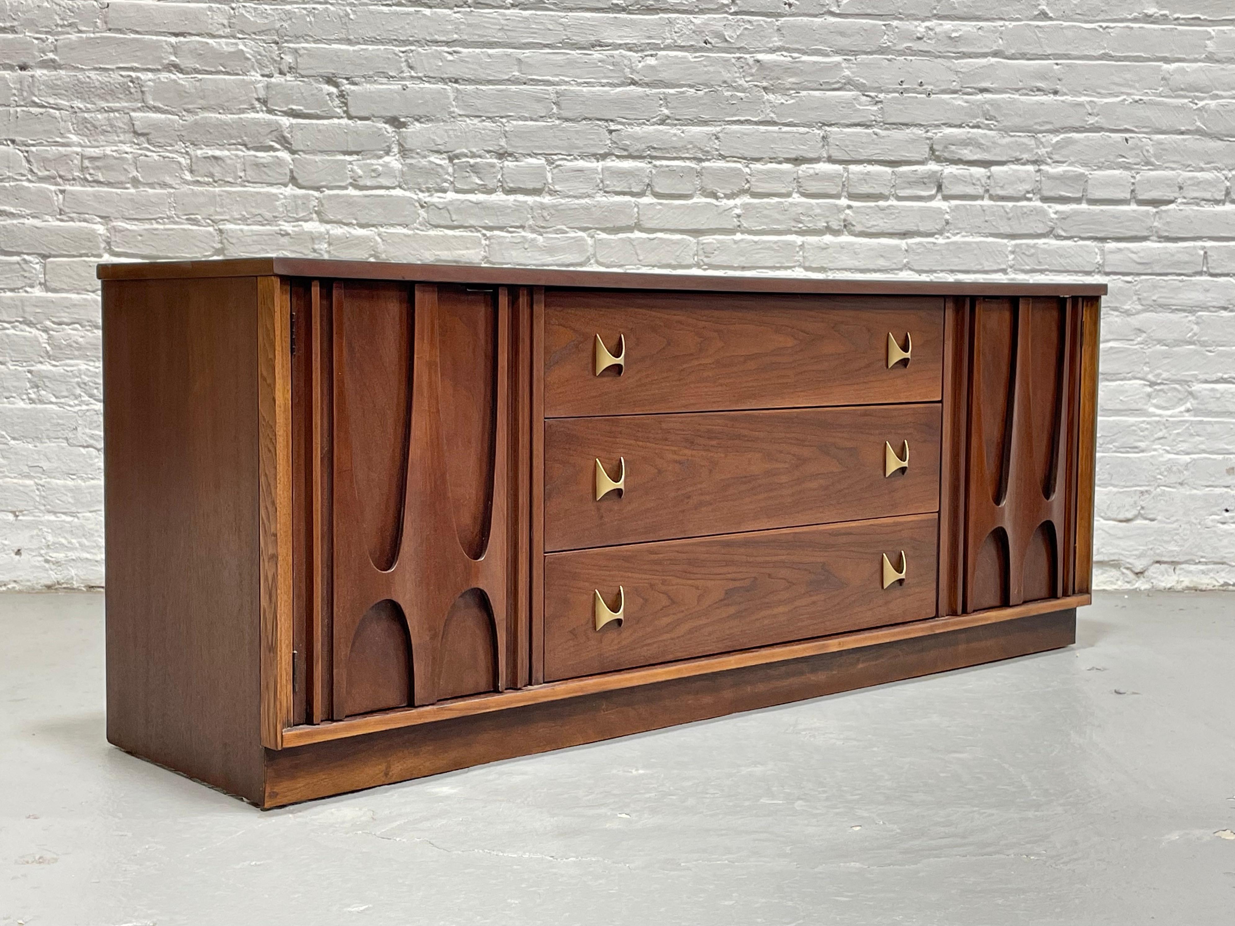 Mid Century Modern Broyhill Brasilia Dresser, c. 1960's. This is a magnificent credenza from the much beloved and voraciously collected Brasilia collection. From the distinctive elongated, inverted sculpted arches to the brass hand pulls, this piece