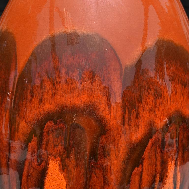 Monumental ceramic lamp in orange and black glaze. Original hardware including a brass harp with wood finial. This lamp is bulbous in form and wider at the bottom and tapers upward to the top. The glaze varies in color from oranges to deep browns.
