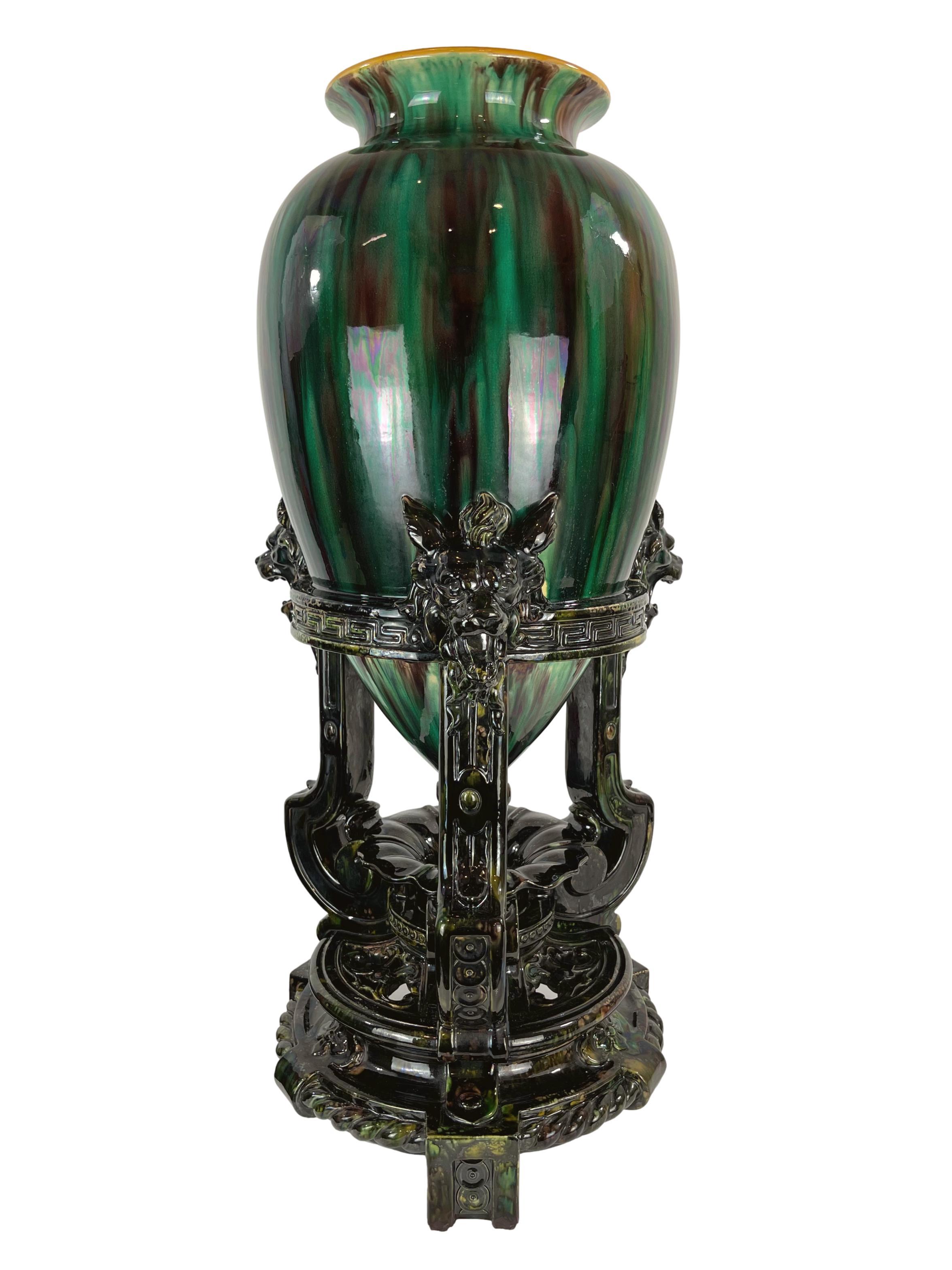 Monumental Minton Majolica Floor Vase, molded as a large Chinese bottle vase glazed in mottled green, brown, and black, banded in yellow, the interior glazed in pink, supported by an integral black glazed tripod base with three fierce beasts-head