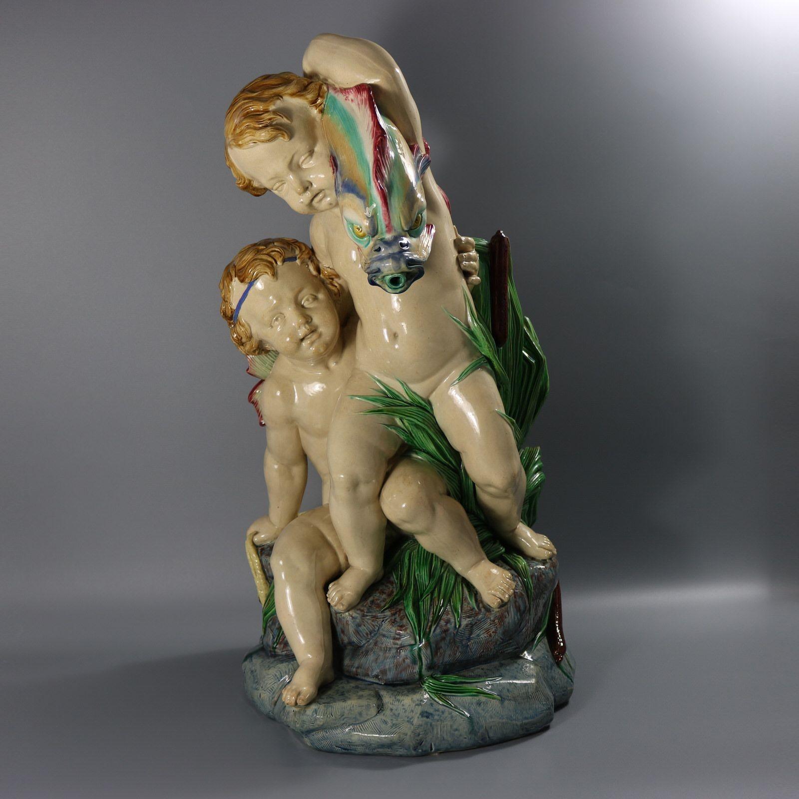 Fontaine en majolique de Minton représentant deux putti sur un affleurement rocheux parmi des joncs. L'un d'eux est assis et tient un filet de pêche. L'autre tient un grand poisson ou un dauphin sur son épaule. La bouche du dauphin forme le bec