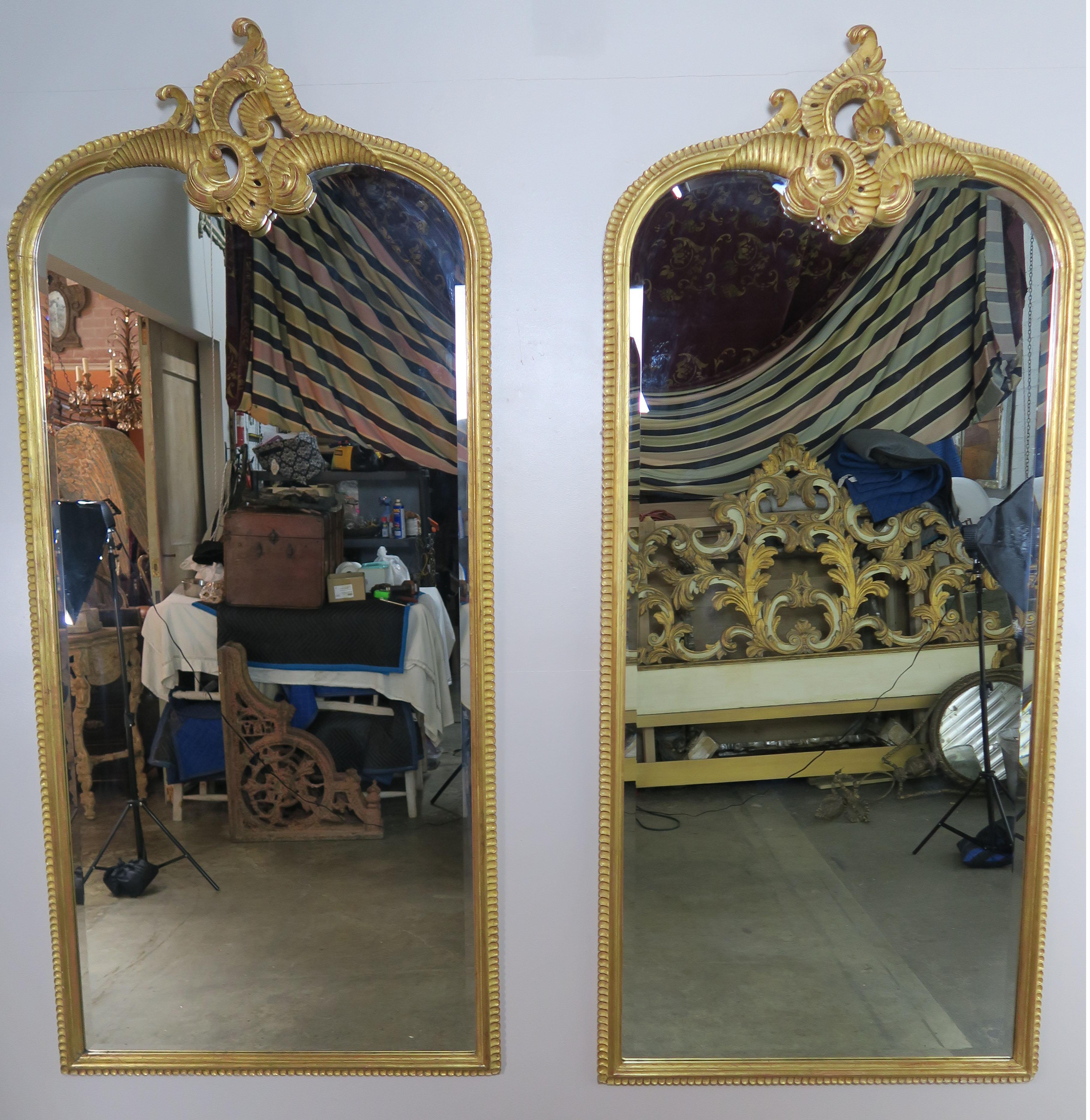 Pair of monumental mirrors carved from wood and finished in a 22-karat gold leaf finish. The mirror has beautiful carved scrolls at the tops of both mirrors with acanthus leaf details and carved detailing around the perimeter of the mirror.
1