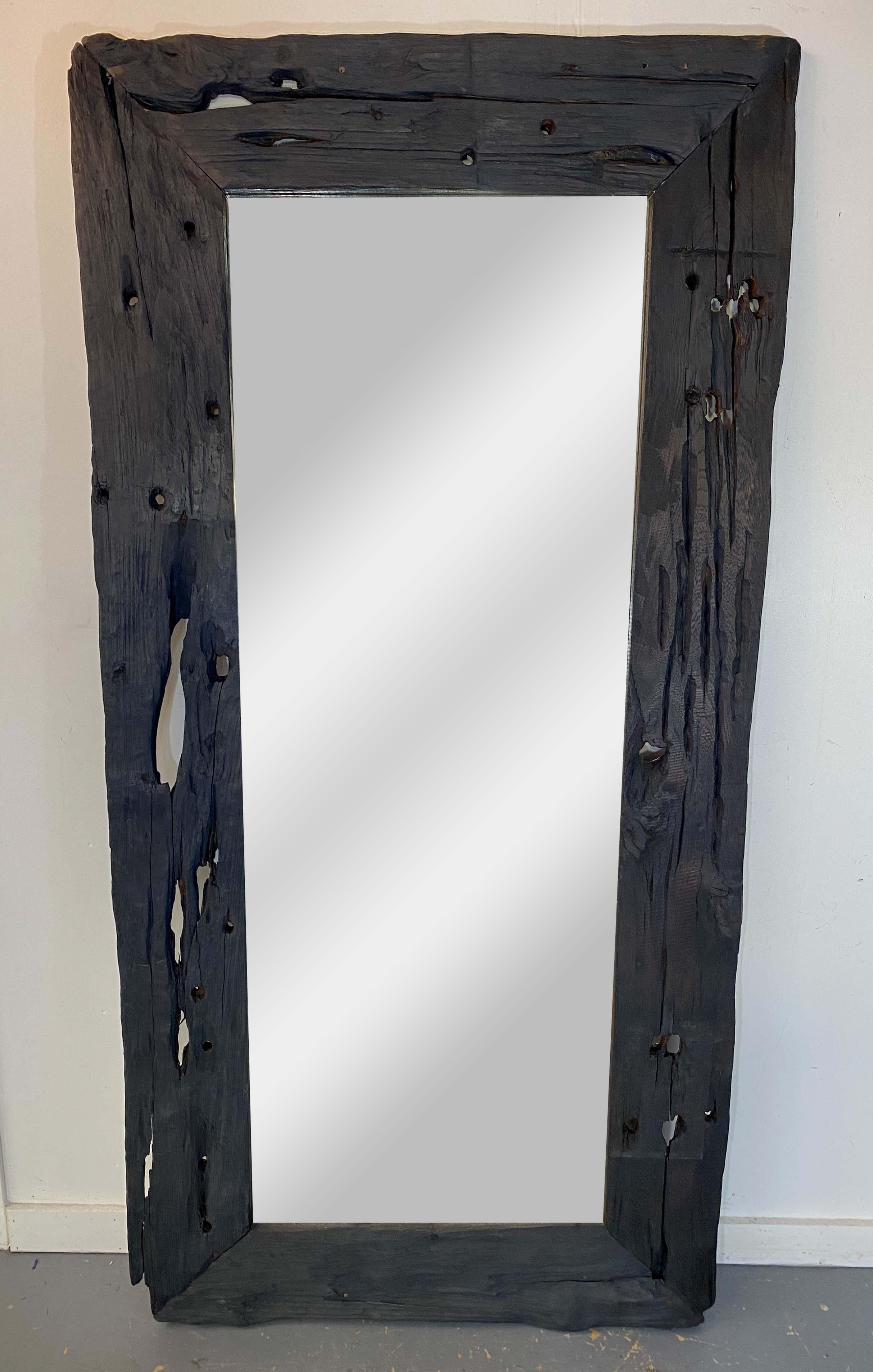 A stylish monumental modern rustic style floor mirror. The stylish mirror is beautiful hand carved of organic wood and shows natural shapes and design adding to its organic flair. The mirror is study and features an onyx , dark gray color. The