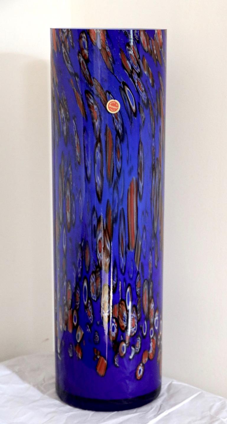 Vase en verre d'art de Murano de taille inhabituelle, avec un fond bleu et des reflets millefiores multicolores. Belle forme cylindrique moderniste, présence impressionnante et état parfait. Ce vase n'est pas signé mais conserve l'étiquette