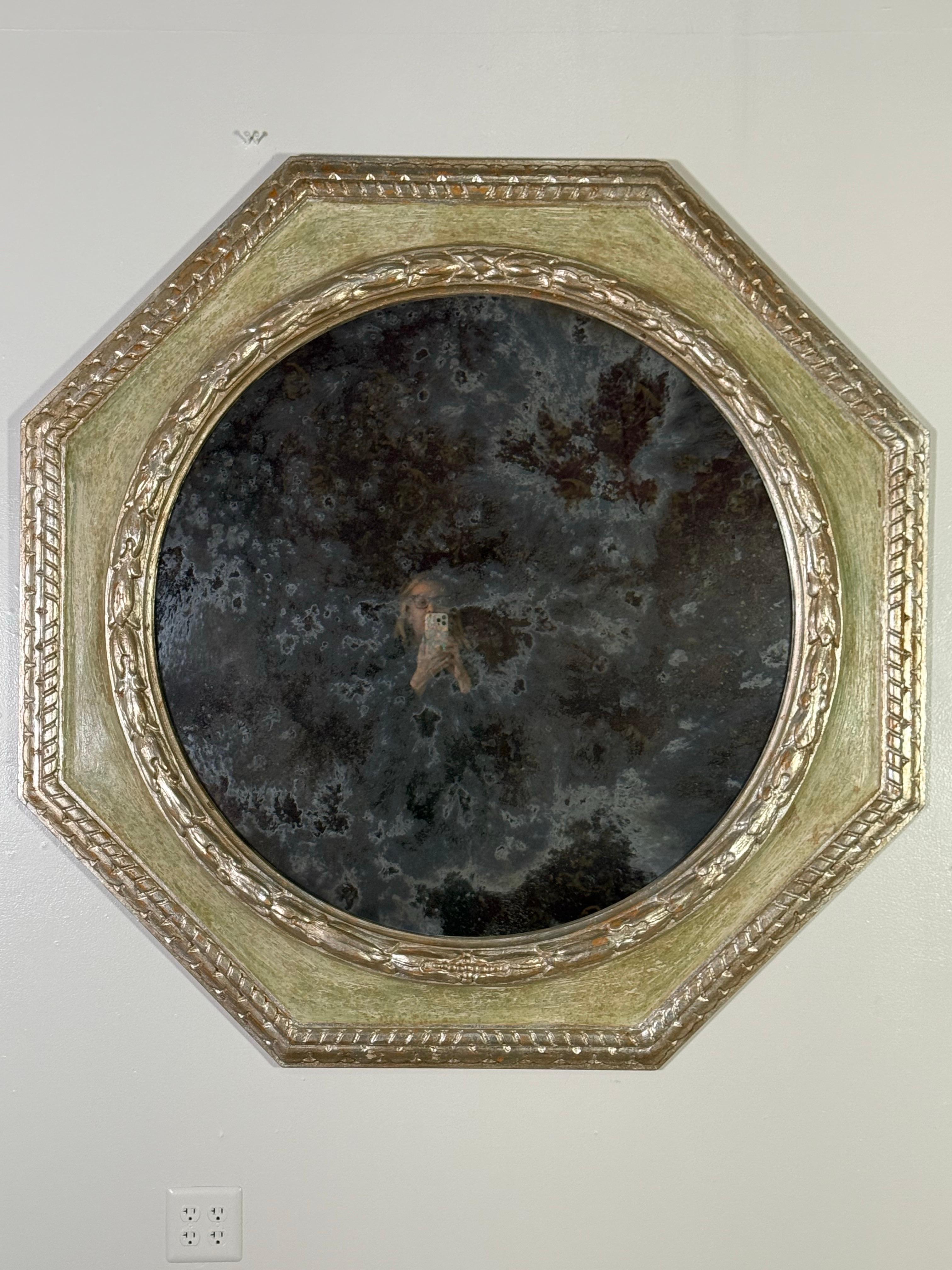 Espejo octogonal monumental con marco de madera pintado a mano y acabado en oro verdoso apagado. El marco está adornado con intrincados detalles dorados, incluidos delicados bordes tallados con motivos clásicos.  El cristal del espejo tiene una