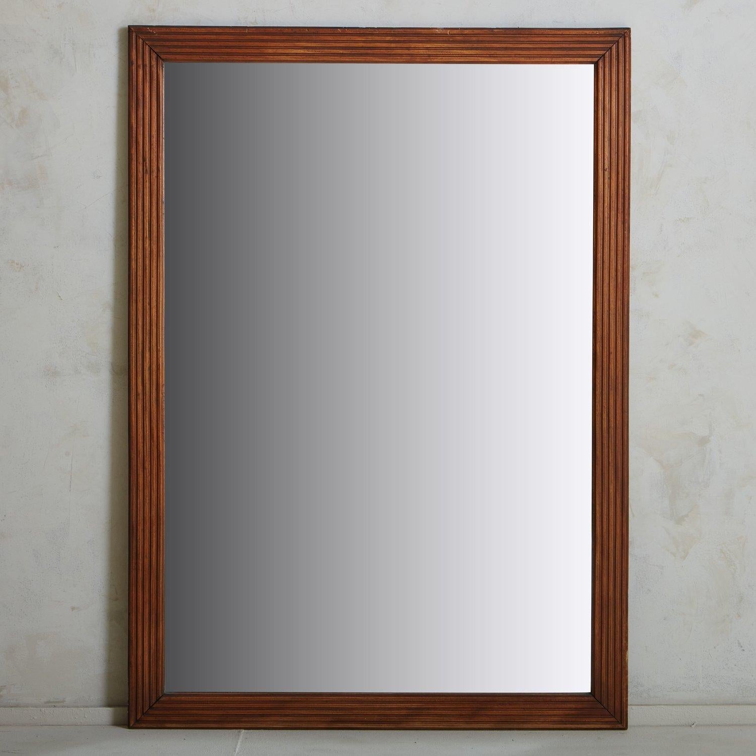 A monumental rectangular French mirror featuring a textured oak frame with beautiful line detailing. This stately mirror has a beautiful patina to the wood frame and time honored wear. It has a wooden backing constructed with six planks. Sourced in