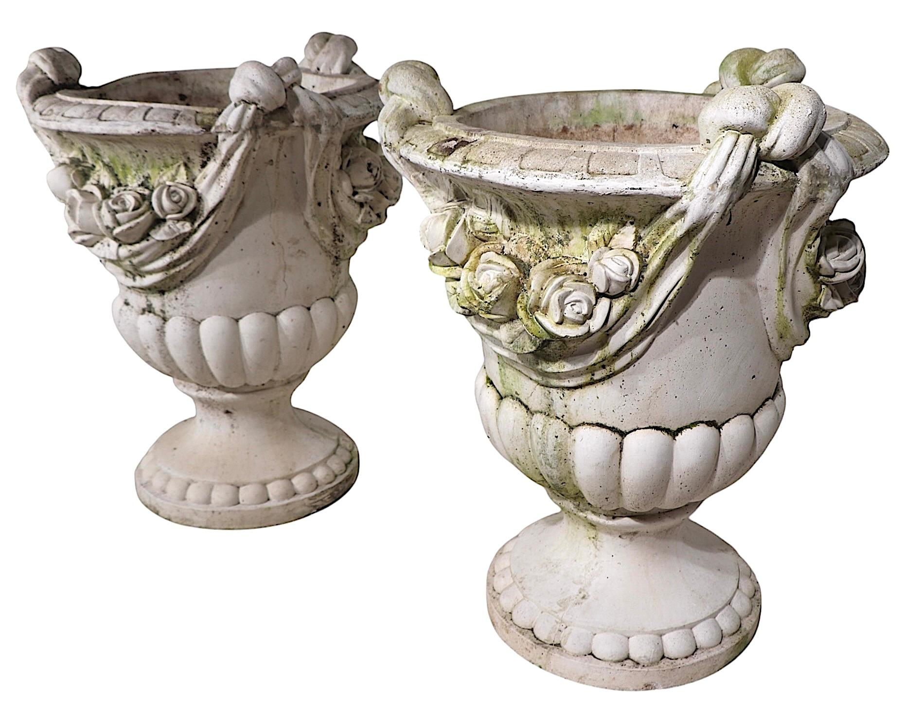 Incredible pair of vintage cast stone urn form planters, in very good original, ready to use condition. The urns feature bold flowers in cast relief with a draped swag surround. The bowl is mounted on a circular plinth base. 
 Both pieces are in