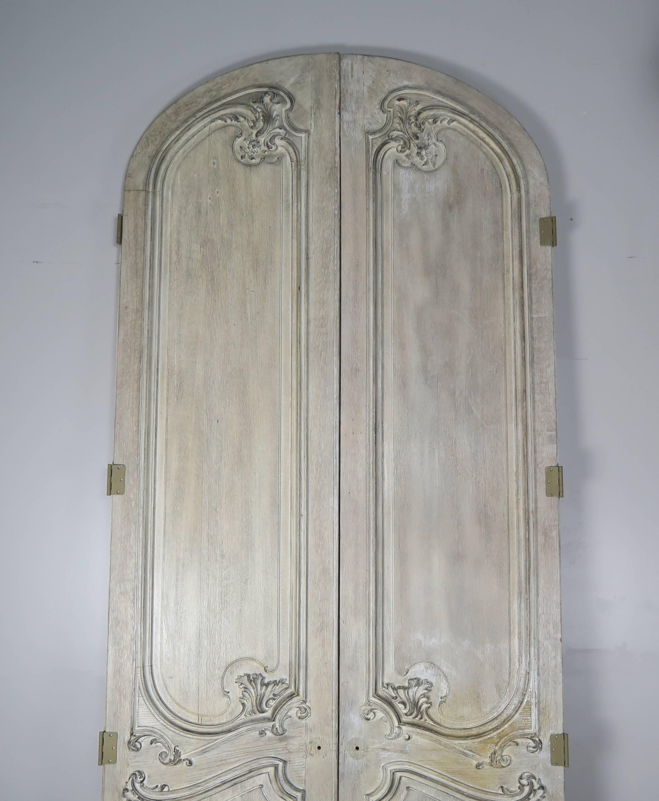 Pair of monumental French carved arched Louis XV style doors with worn painted finish.