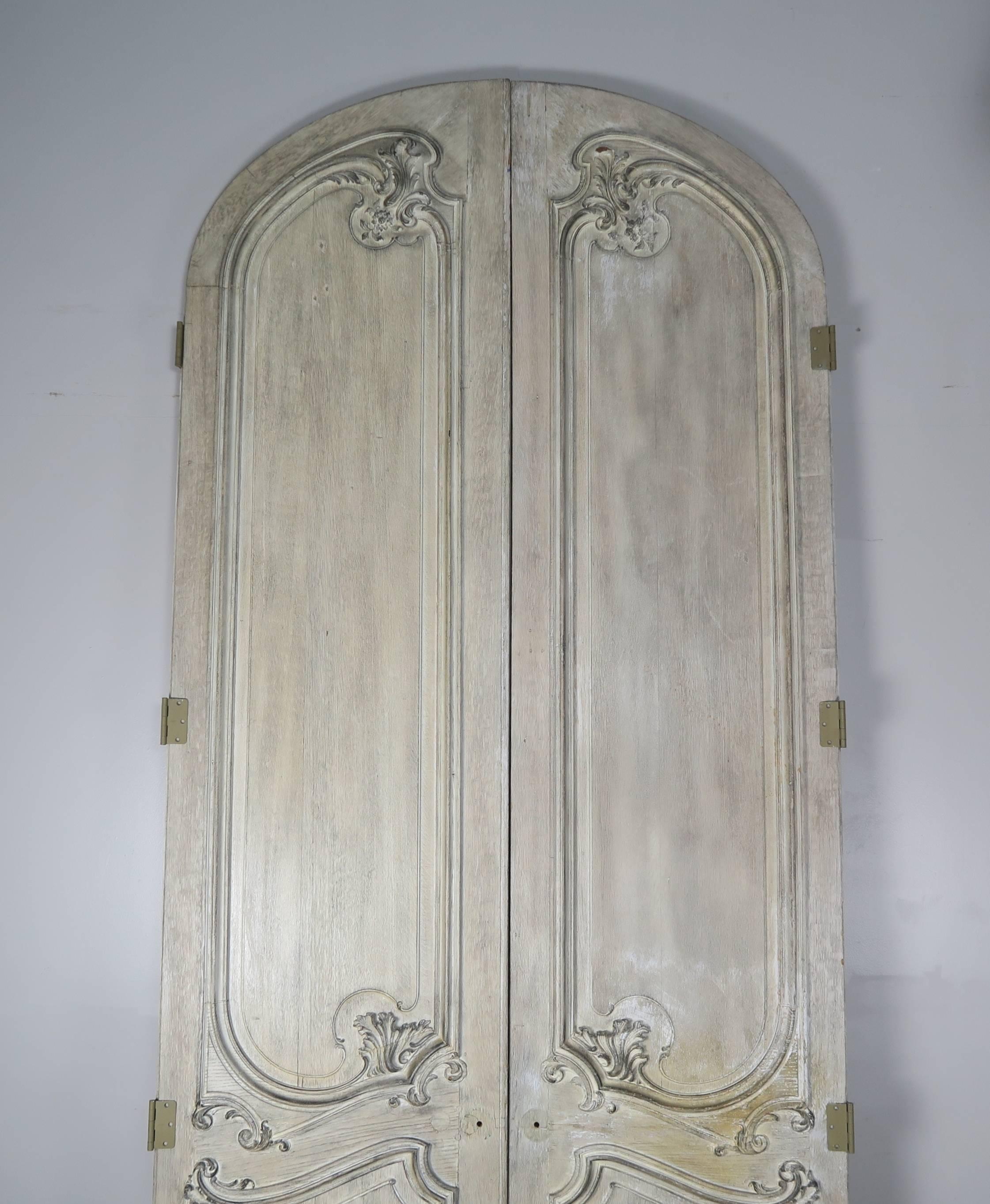 Paire de portes monumentales françaises sculptées et cintrées de style Louis XV avec une finition peinte usée.