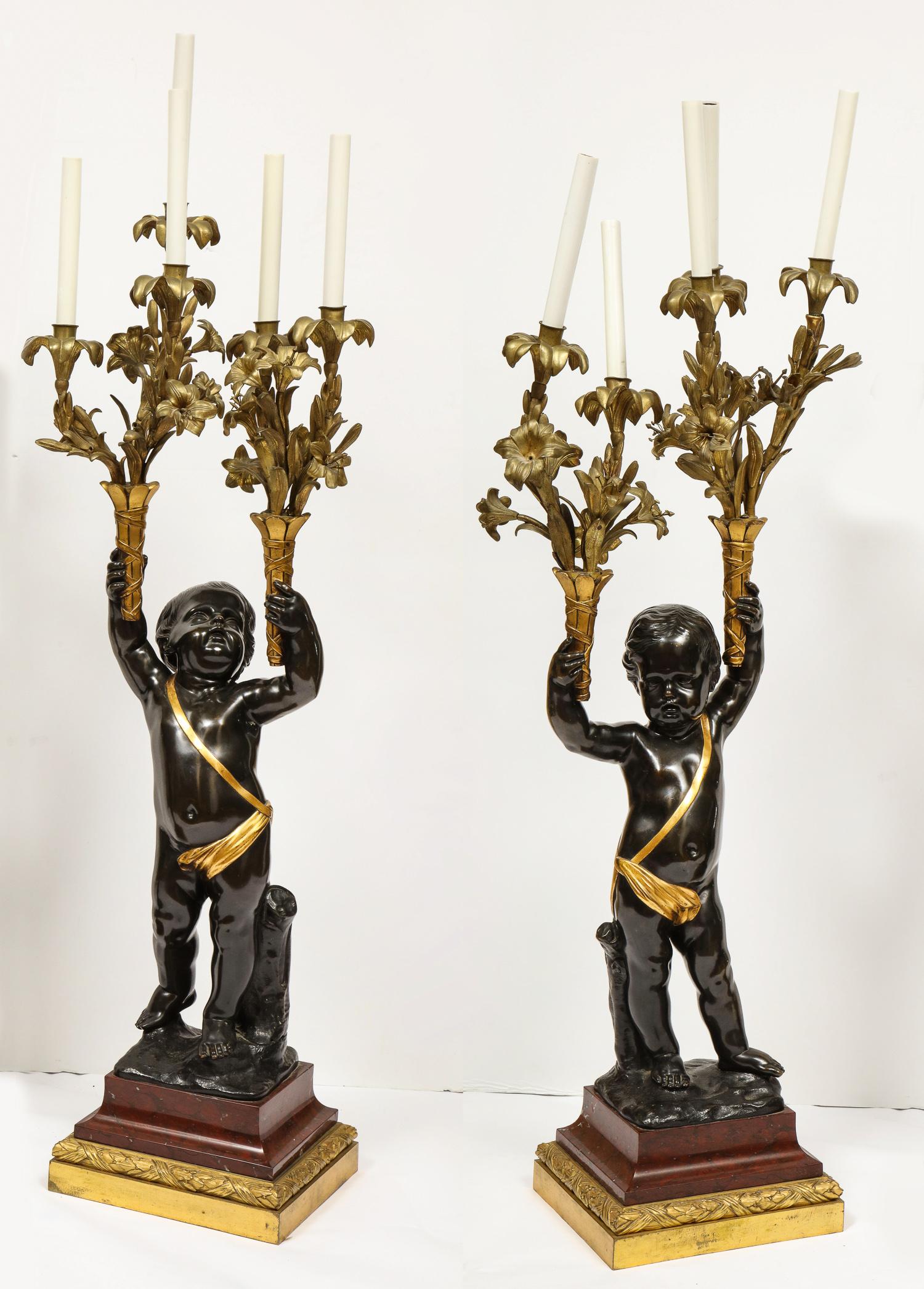 A monumental pair of French gilt and patinated bronze and rouge marble five-light candelabra / torchère / lamps, circa 1870.

Attributed to Henry Dasson, Paris.

Depicting two cherubs holding the candelabra / torchiere in each hand, on square