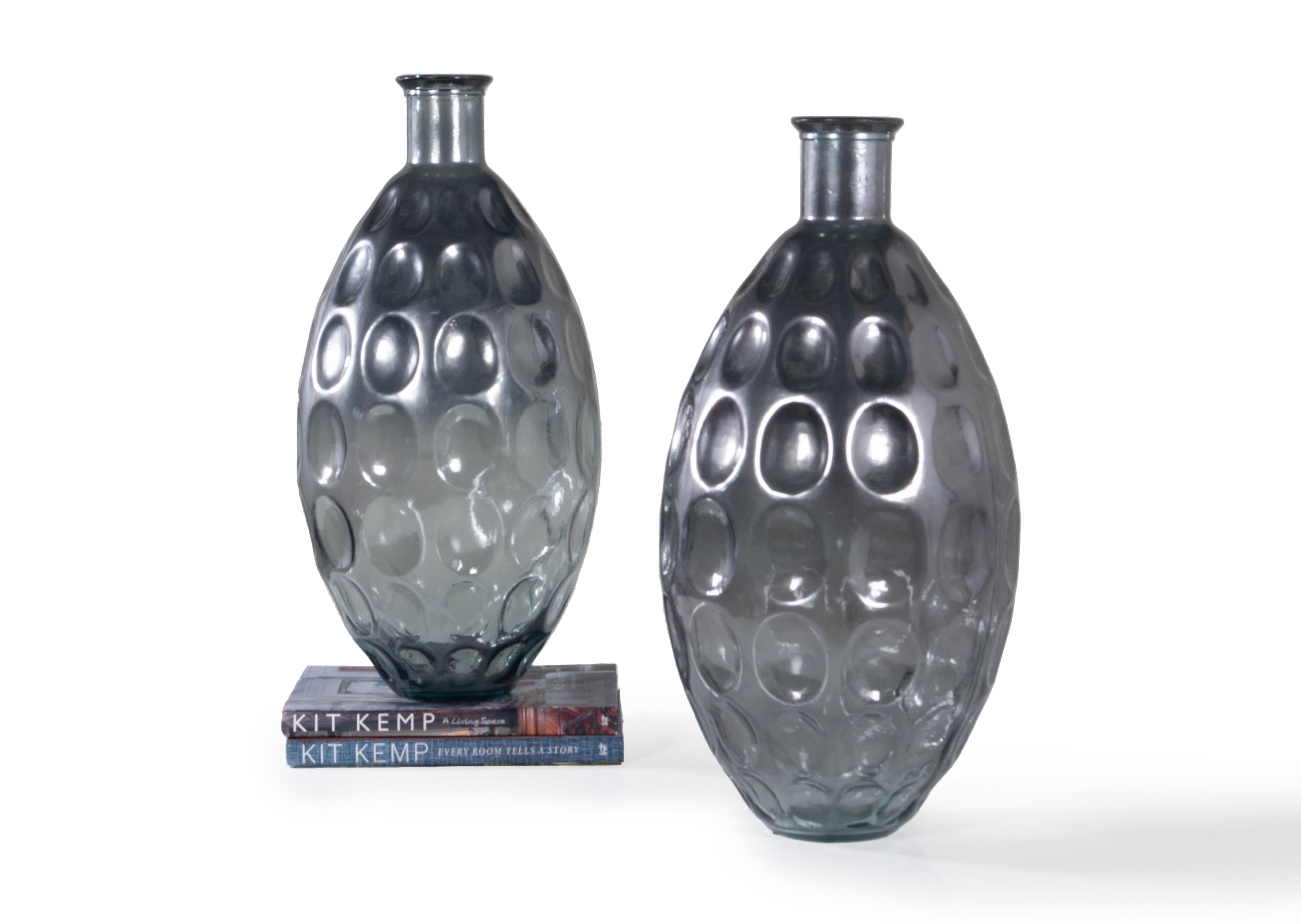 Add luster to any space with this pair of monumental pressed glass vases. These vases feature a slightly metallic finish atop a stone grey blue hue and an inverted oval impression throughout. The narrow mouth of this pair of monumental vases