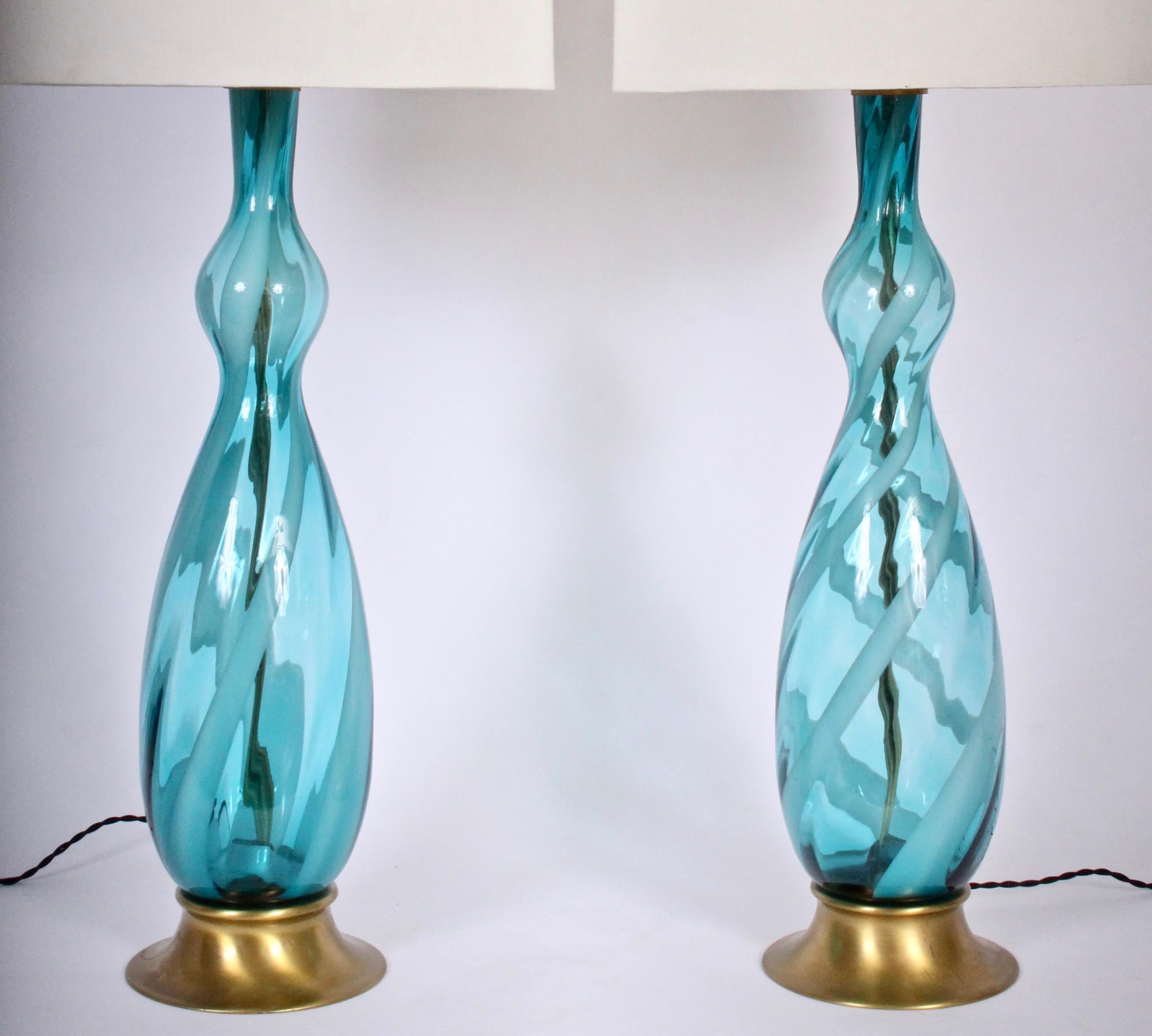 Statuesque pair of Italian sea ocean blue and white frost whirl Murano glass table lamps. Featuring a tall hand crafted bottle form, Pale white candy cane striping on a splayed brass base. Shades for display only (13 H x 13.5 D top x 14 D bottom).
