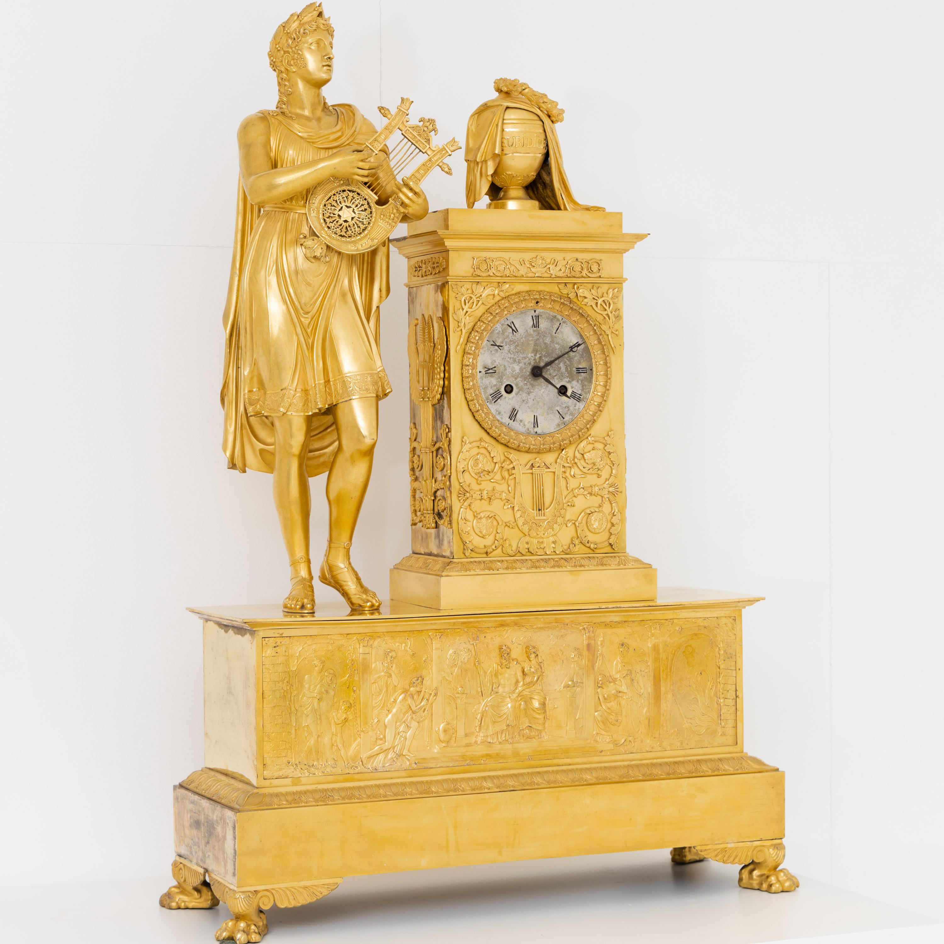 Very large pendule made of fire-gilded bronze with a fully plastic representation of Orpheus with his lute. The clock case is crowned by the urn of Eurydice. On the wide plinth multi-figured representation with Hades enthroned in the centre and