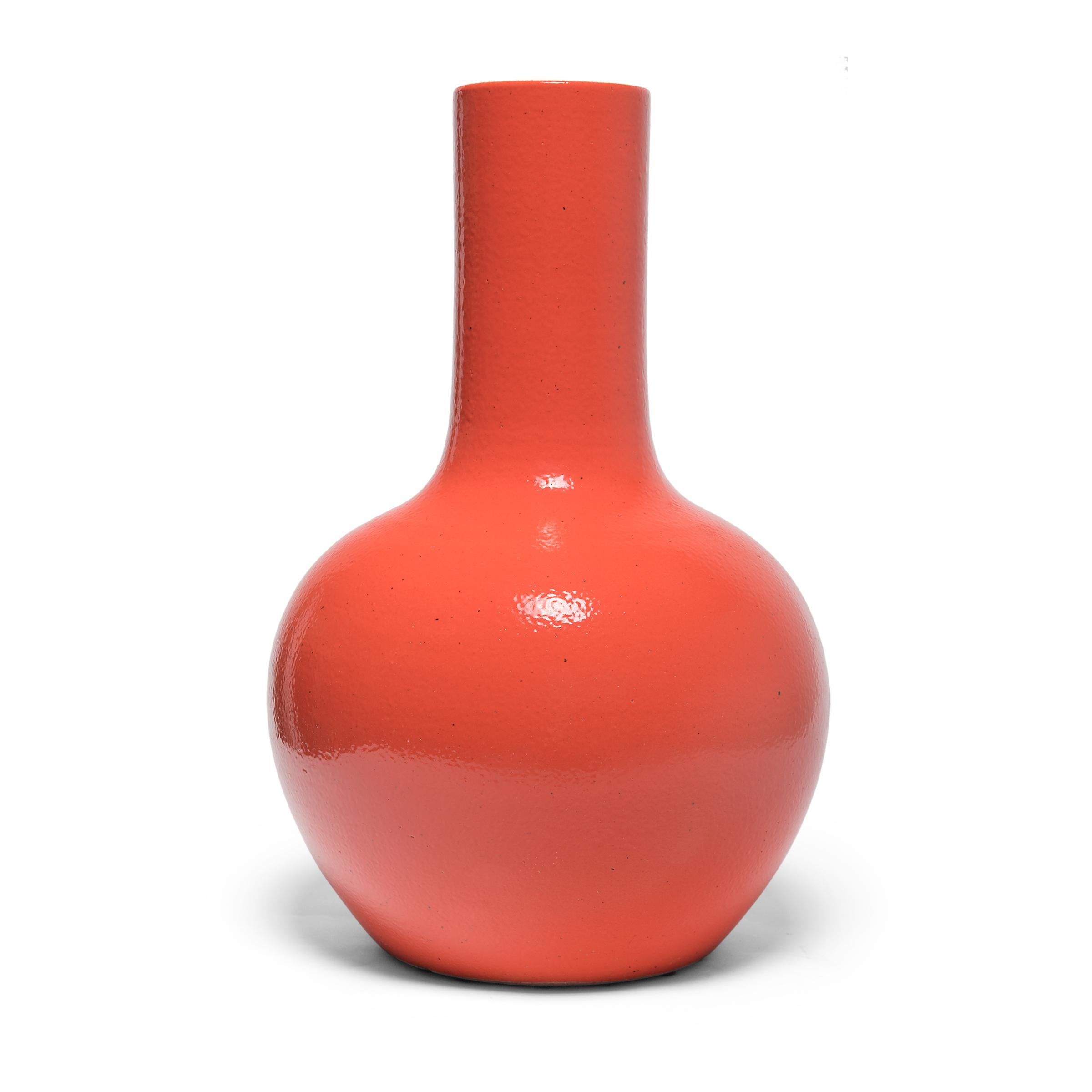 Drawing on a long Chinese tradition of monochrome ceramics, this tall gooseneck vase is glazed in vibrant persimmon-orange glaze. The vase features a rounded, globular body and a narrow cylindrical neck, a classic form known as 'tianqiuping' or