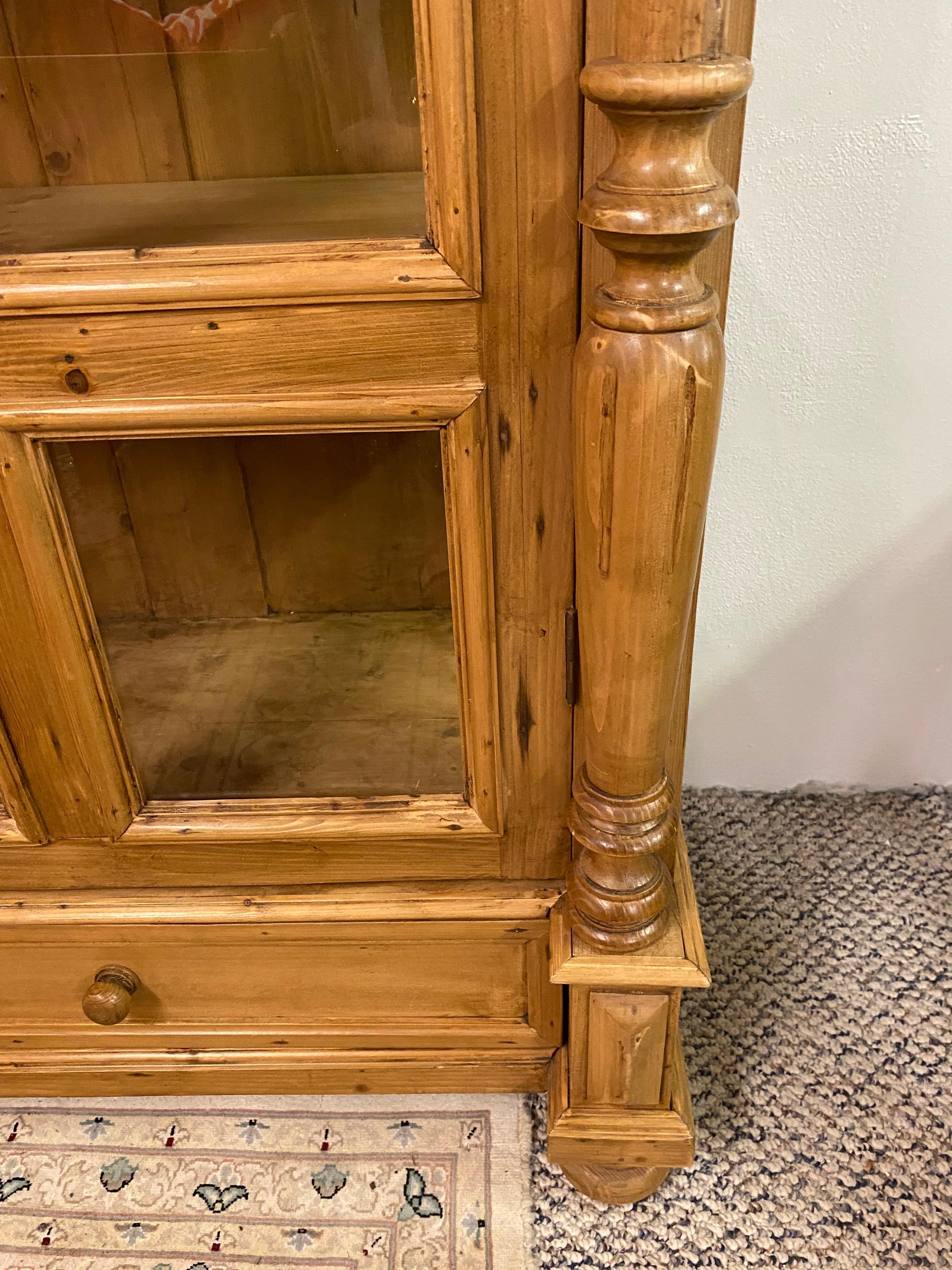 Impressive very large pine cabinet of European origin having glass panes on double doors, decorative crown, and fluted columns. There are three interior shelves plus two drawers side by side at the bottom of the cabinet which provide wonderful