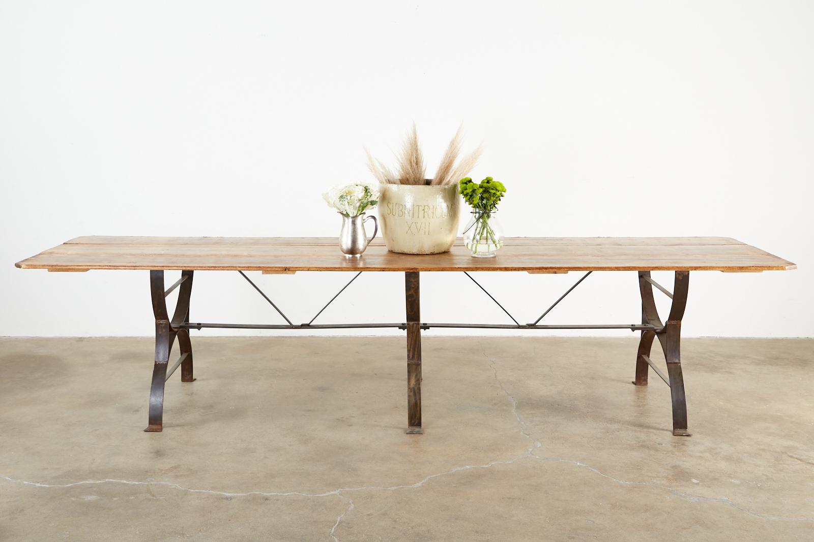 Monumental harvest table or farmhouse dining table featuring a triple leg cast iron trestle base measuring nearly 11 feet long with a rustic pine plank top. The cast iron Curule leg bases are conjoined by a long cross stretcher having a decorative