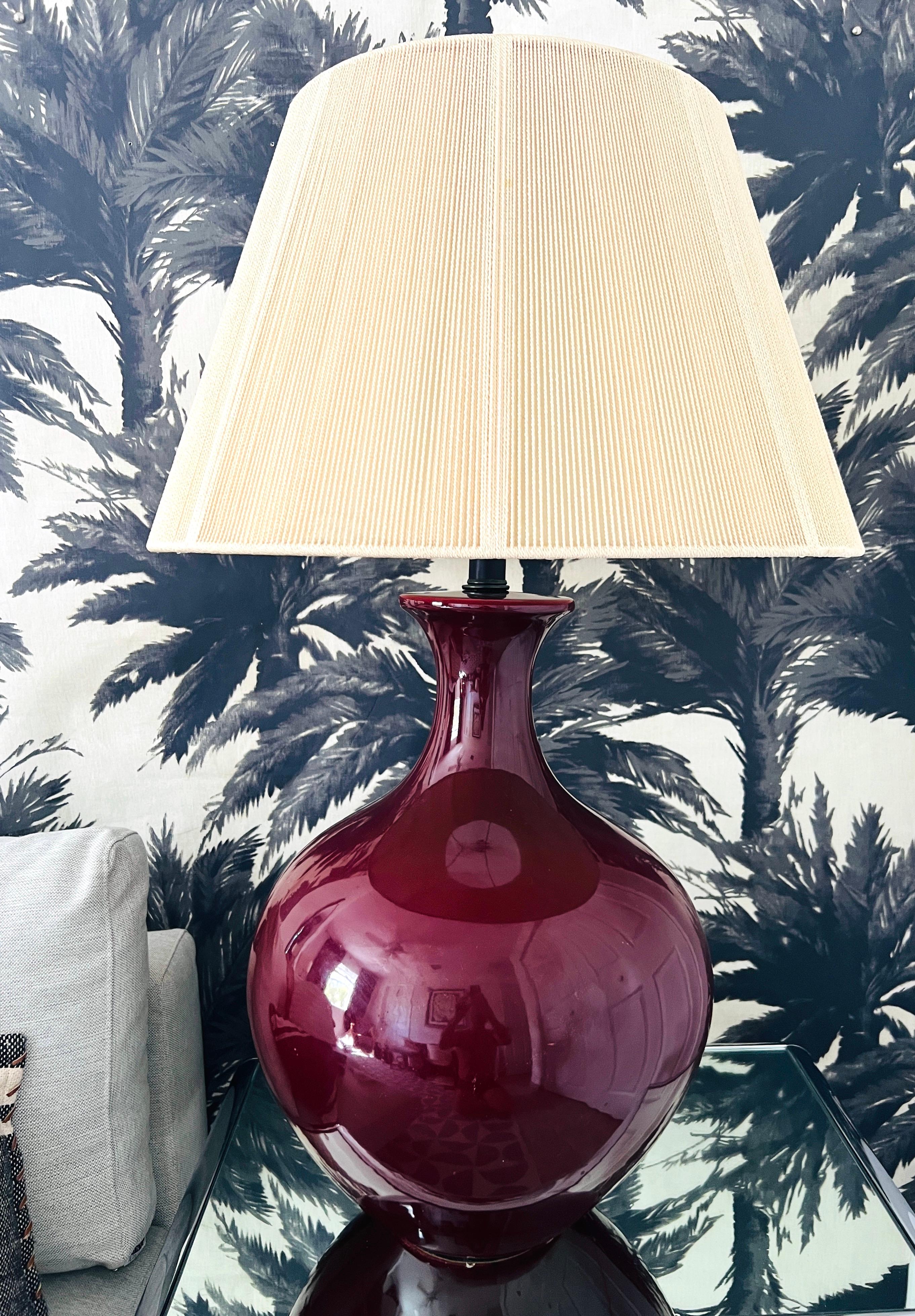 1970's monumental oxblood lamp in a deep red burgundy glazed porcelain. The Chinese inspired design features a very large bulbous base with a sinuous form and tapered stem. Includes original large-scale cream colored string shade. Chic and