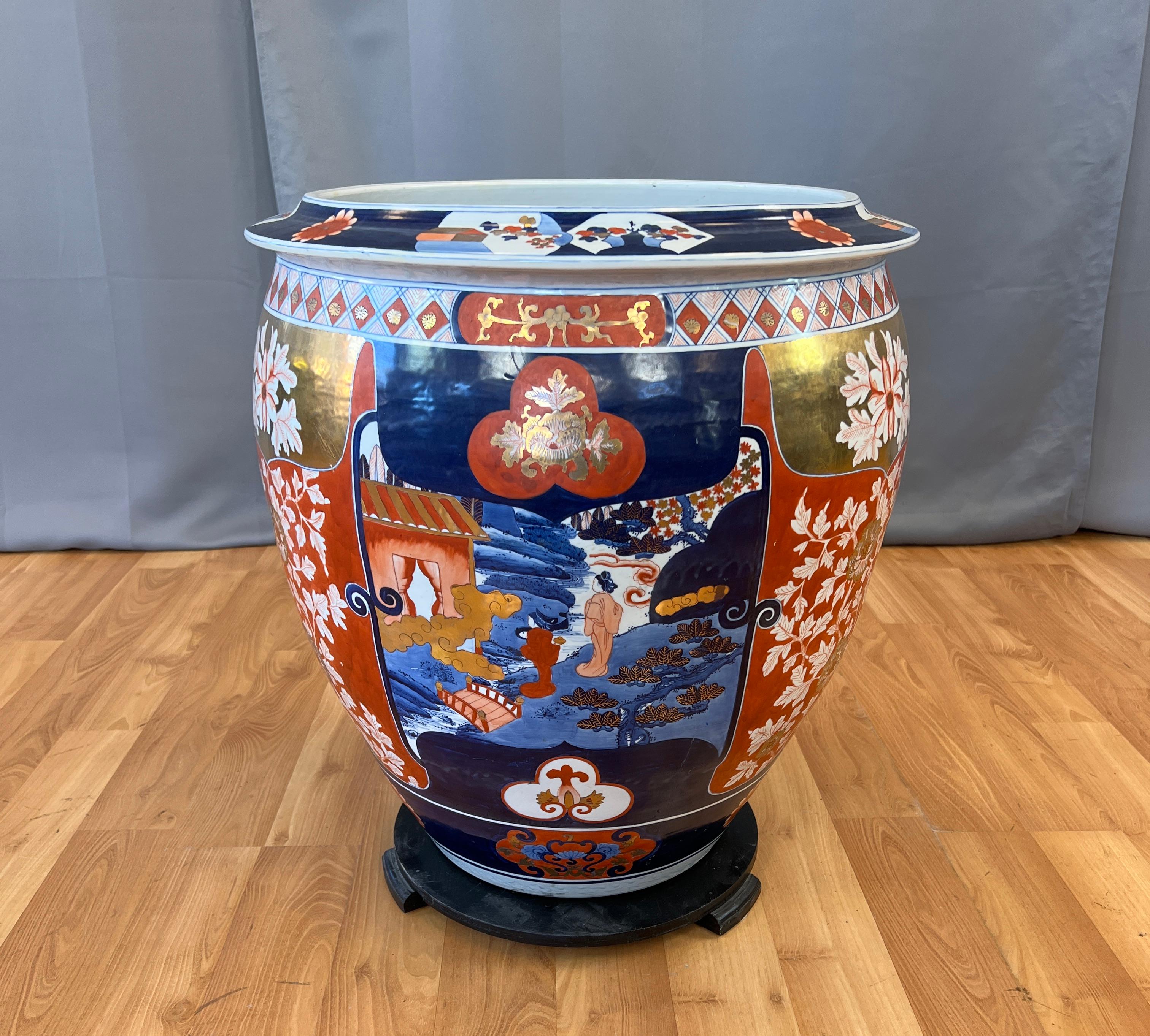 Offered here is a monumental Japanese Imaxi porcelain jardiniere. 

Wonderful colors have been used, blue, both dark and light, gold, reds and white, depicting scenes of a pair of woman walking along a creek above a traditional Japanese bridge, with