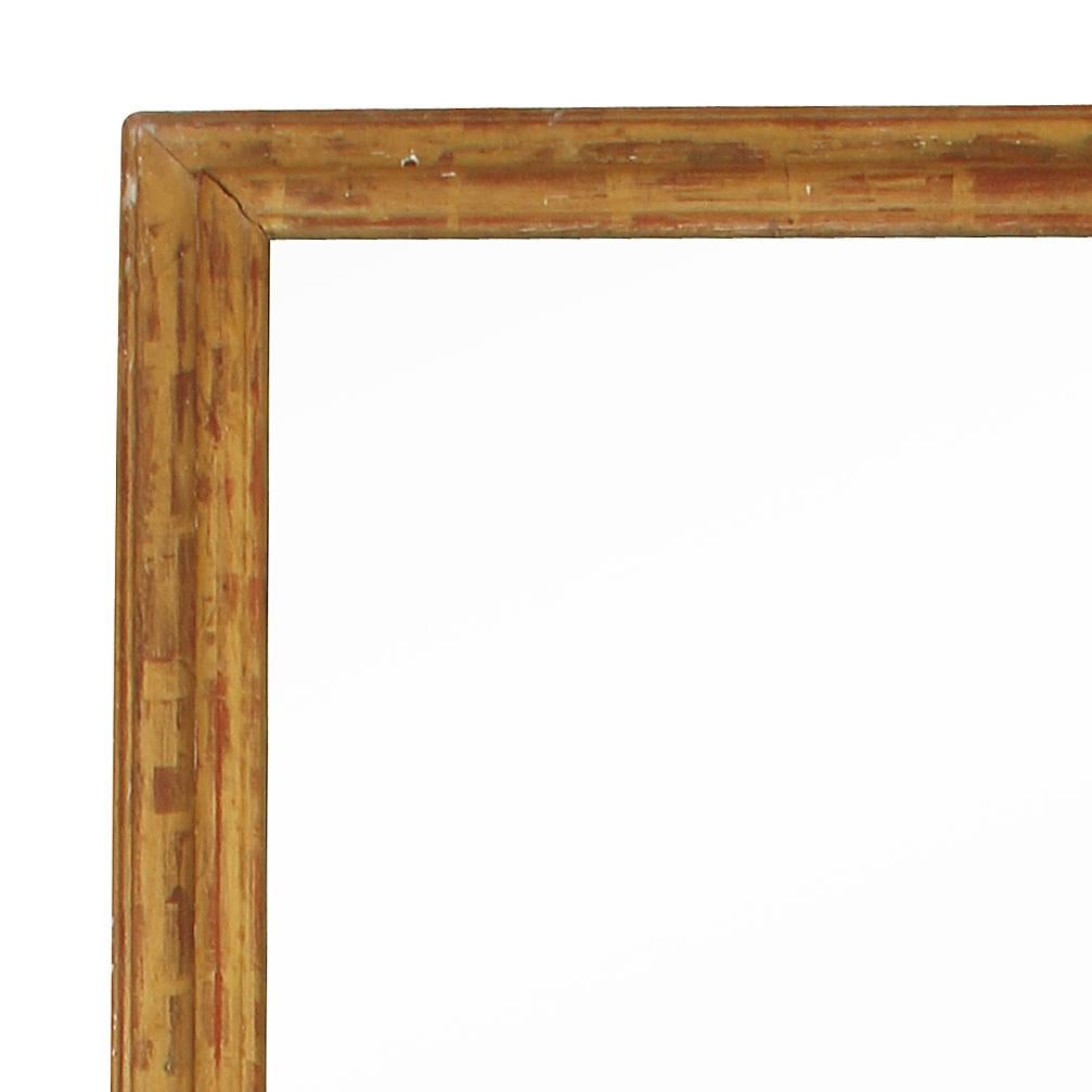 A monumental rectangular gilt and carved wood mirror.  The tall,  narrow mirror has a red underglaze on the beautiful giltwood carved frame.  An important mirror for a grand space.