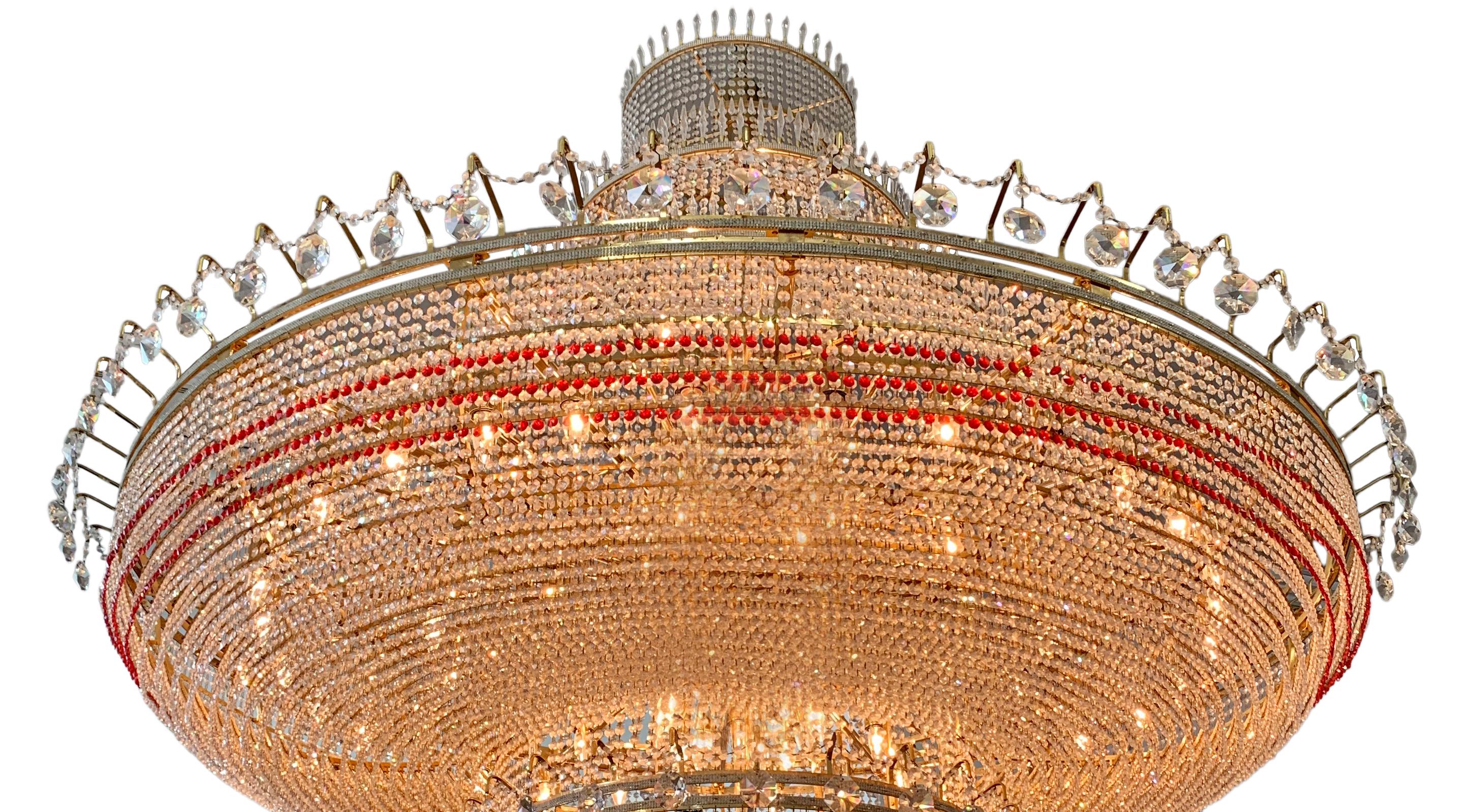 This magnificent continental palace-size chandelier, with 7 x 7 feet dimensions, is decorated with clear and red cut crystals mounted with gilt bronze. A beautiful neo-classical  chandelier with a cone-shaped end where most of the red cut crystals